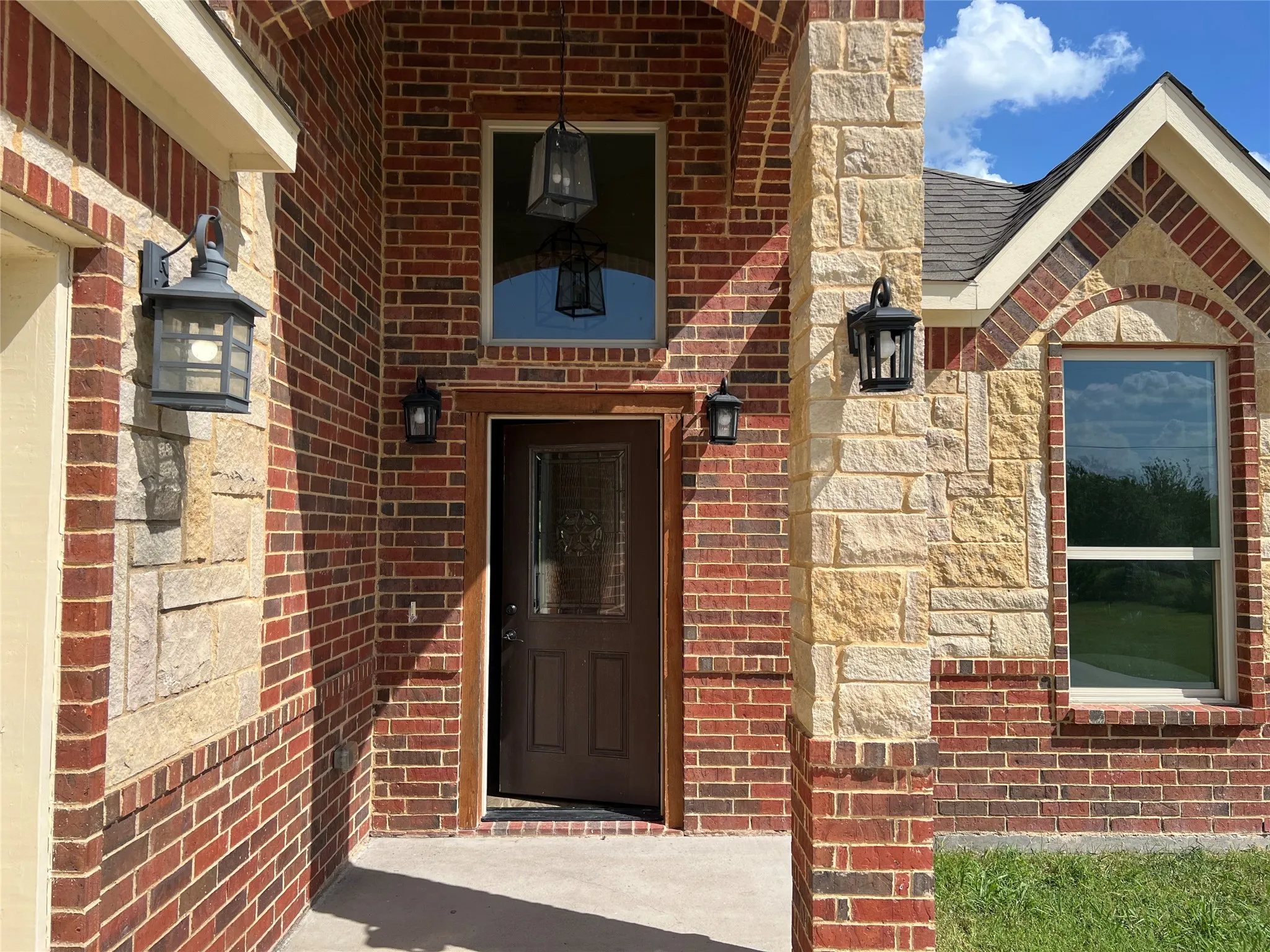Brick and stone facade featuring a dark wood-finish front door with an integrated window, two exterior sconces, and an overhead decorative lantern