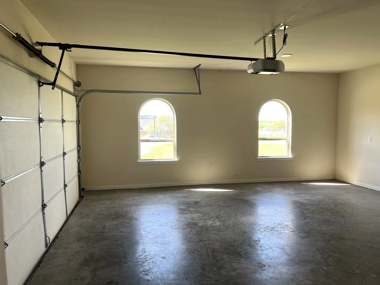 Attached garage with concrete flooring, two arched windows, a sectional garage door, and an automatic garage door opener