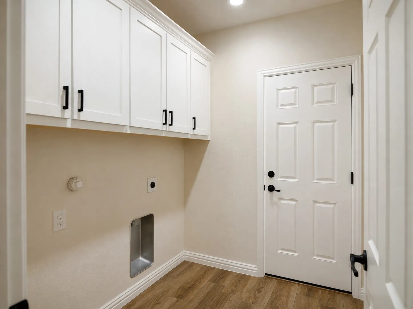 White shaker-style cabinetry with black hardware, wood-finish flooring, and a six-panel door with black hardware