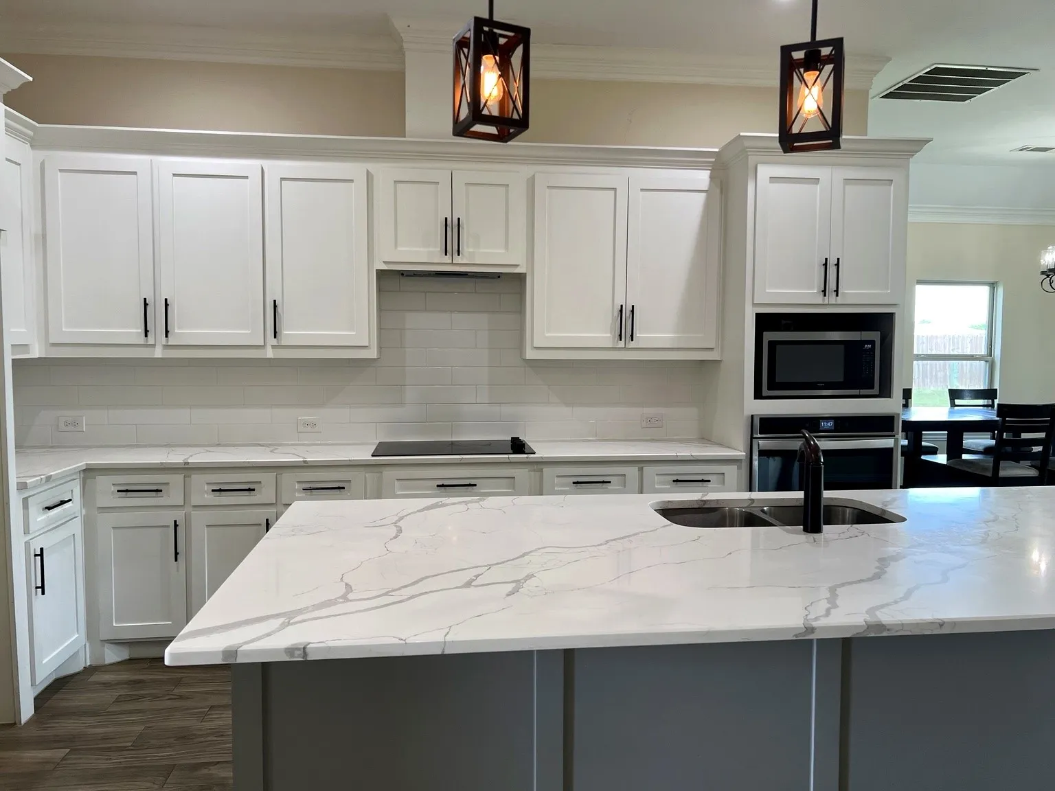 Kitchen with white shaker cabinetry, white subway tile backsplash, white countertops with grey veining, and a central island with an undermount sink
