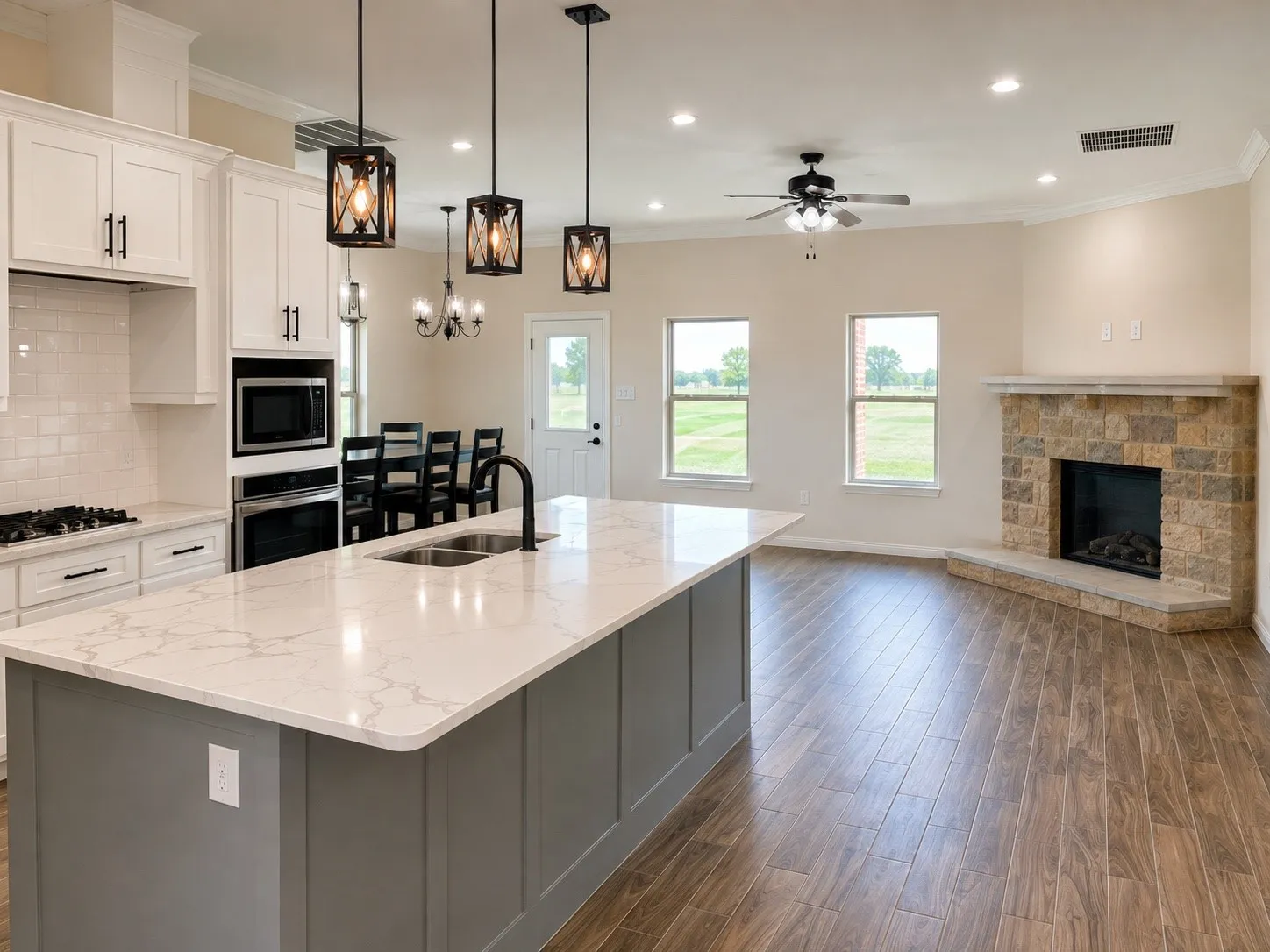 Spacious kitchen with a large island, white cabinetry, integrated stainless steel appliances, and wood-finish flooring extending to a living area with a stone fireplace