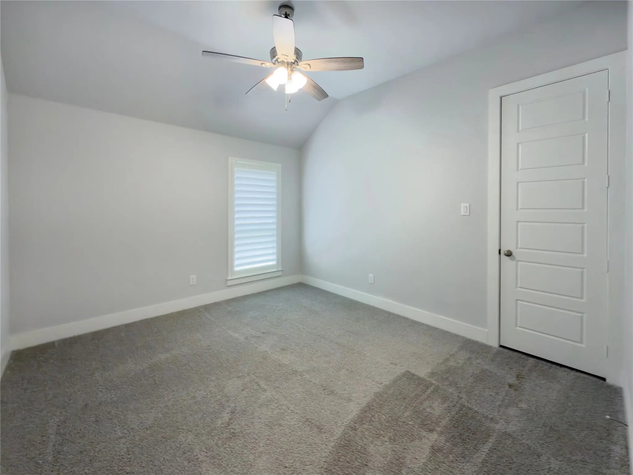 Carpeted room featuring a ceiling fan, a window with horizontal blinds, a paneled door, and white baseboards