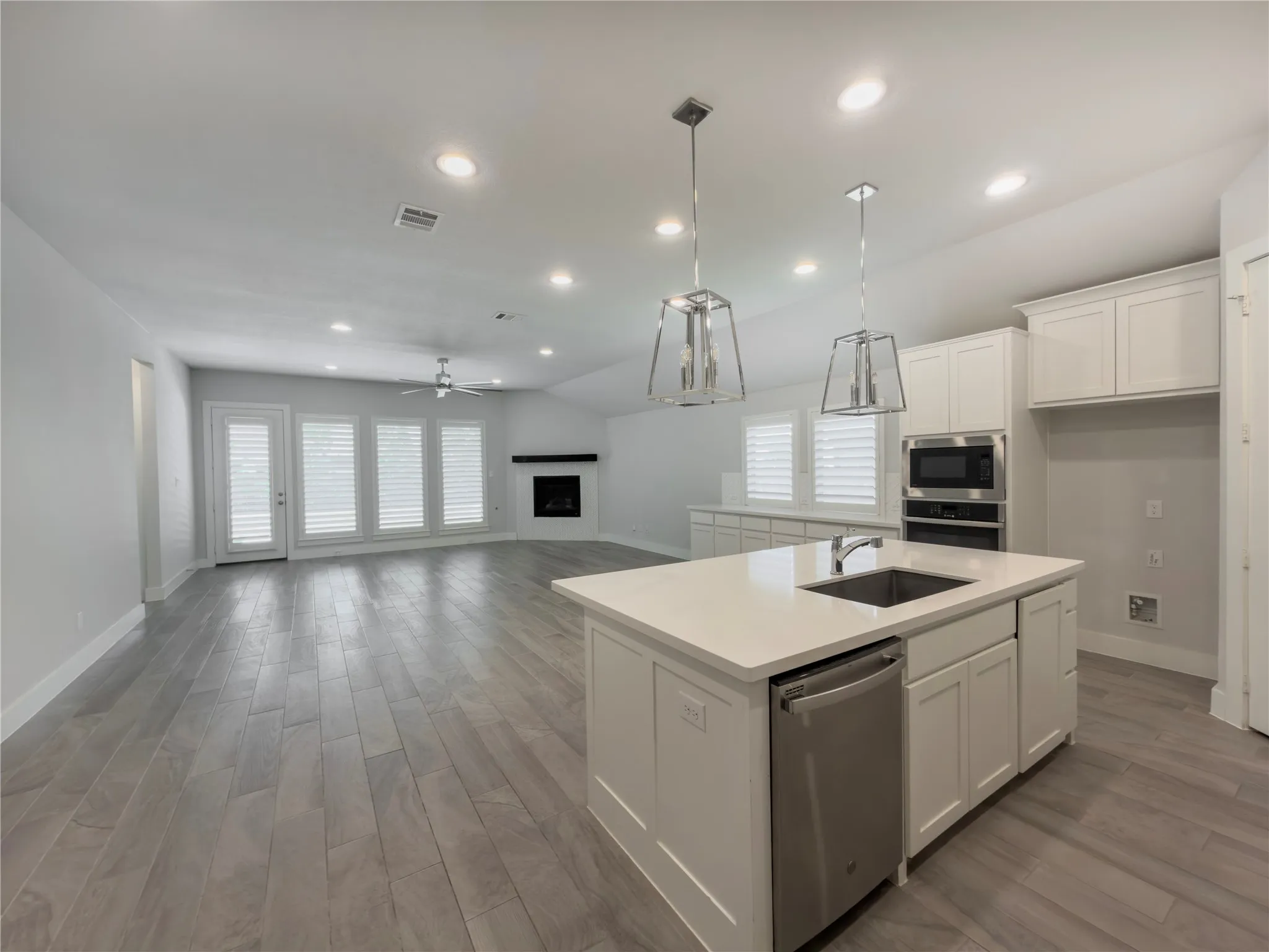 Open-concept space featuring a kitchen island with sink and integrated dishwasher, recessed lighting, and wood-finish flooring