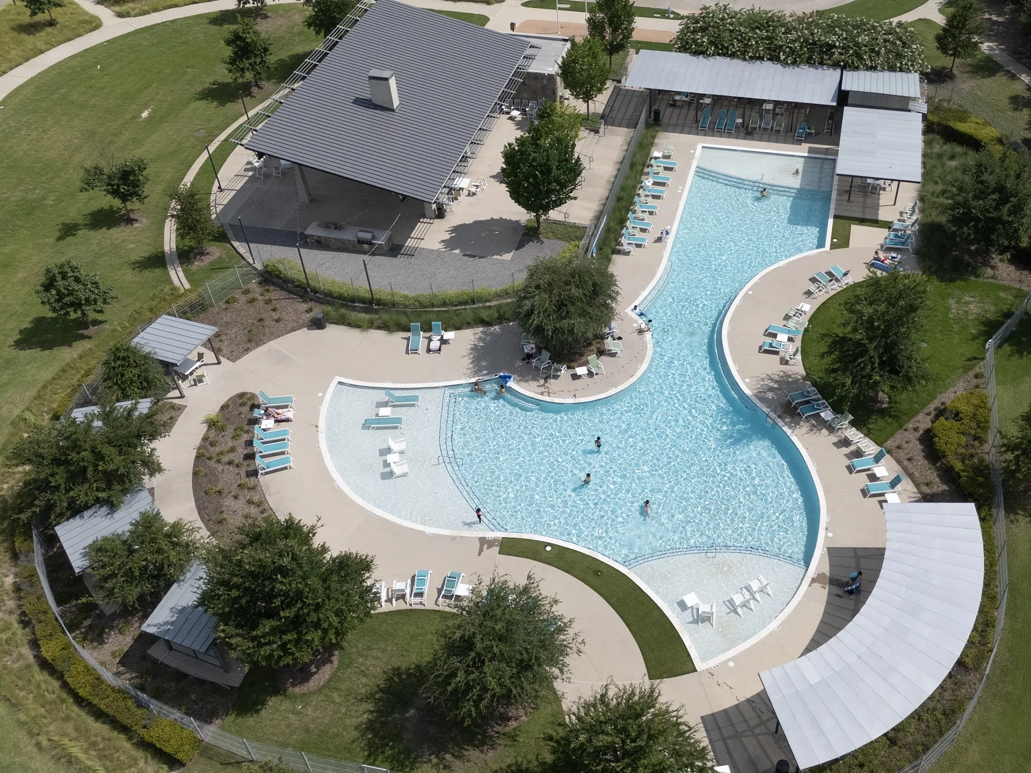 Resort-style pool area featuring a freeform swimming pool with integrated tanning ledges, extensive surrounding concrete decking, and multiple shaded lounge areas