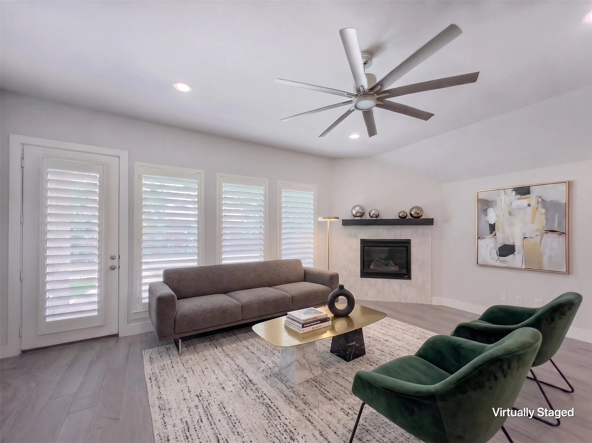 Vaulted ceiling living area featuring wood-finish flooring, a contemporary fireplace with a dark mantel, and multiple windows with plantation shutters