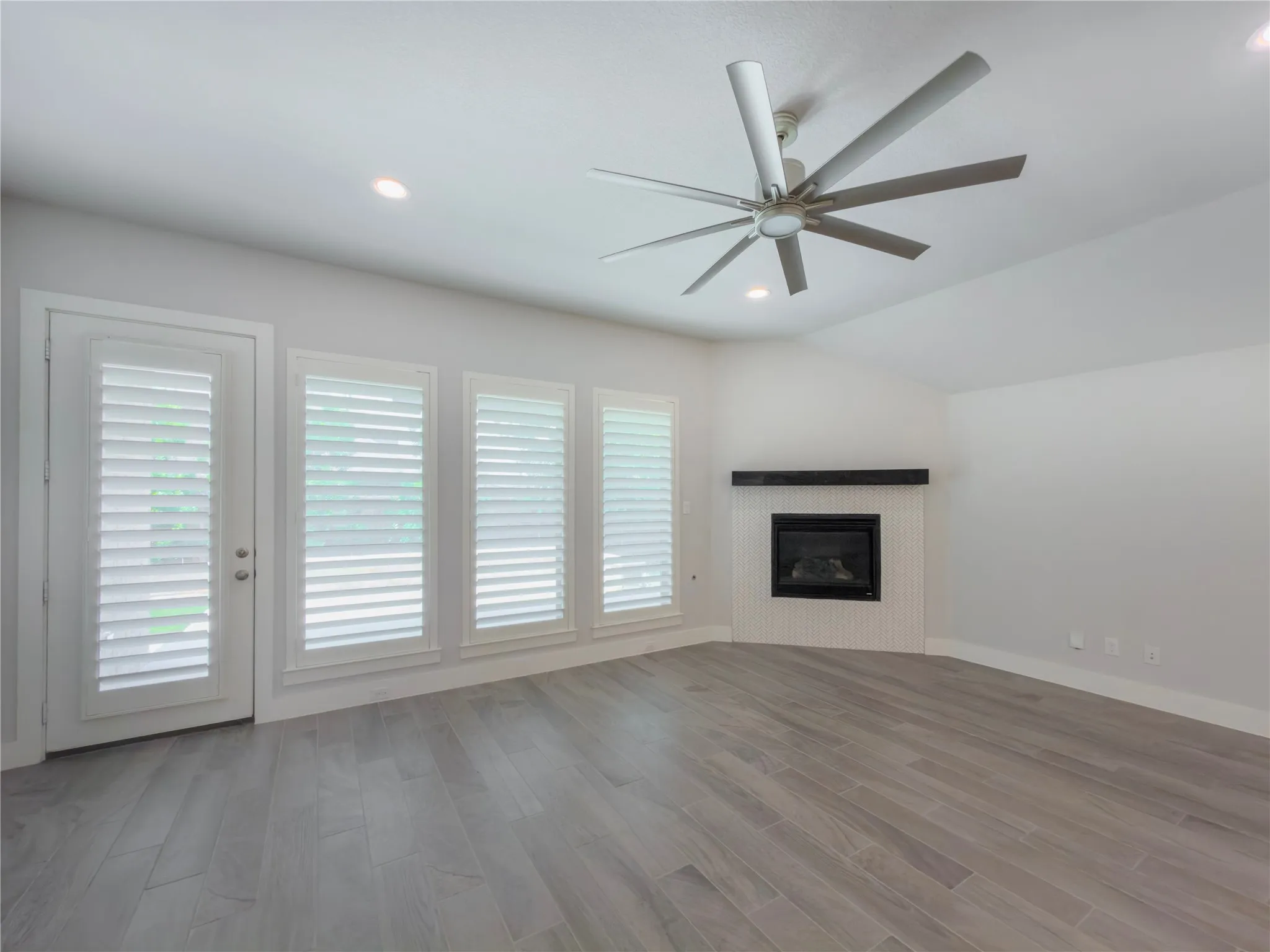 Living area featuring wood-finish flooring, a corner fireplace with a black mantel, an angled ceiling, recessed lighting, and a multi-blade ceiling fan