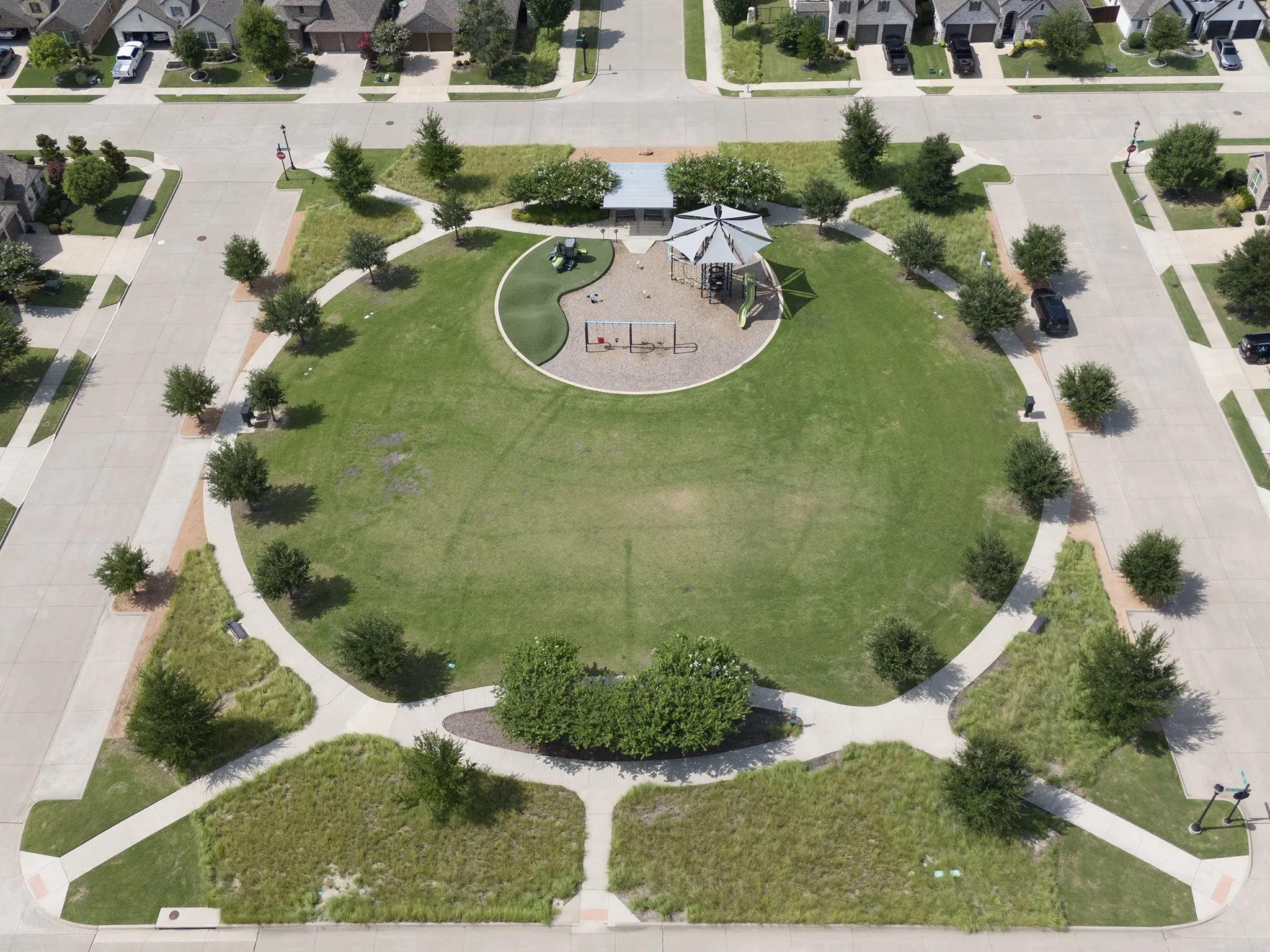 Central green space featuring a playground with a sunshade, surrounded by paved walking paths and mature landscaping