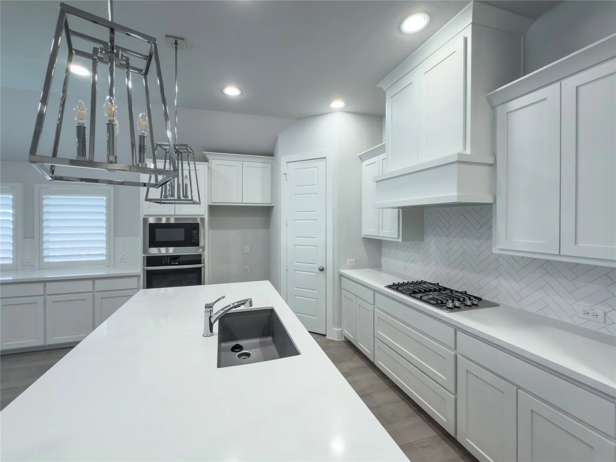 Spacious kitchen featuring an expansive island with an undermount sink, white shaker cabinetry, stainless steel appliances, a gas cooktop, and herringbone-patterned tile backsplash