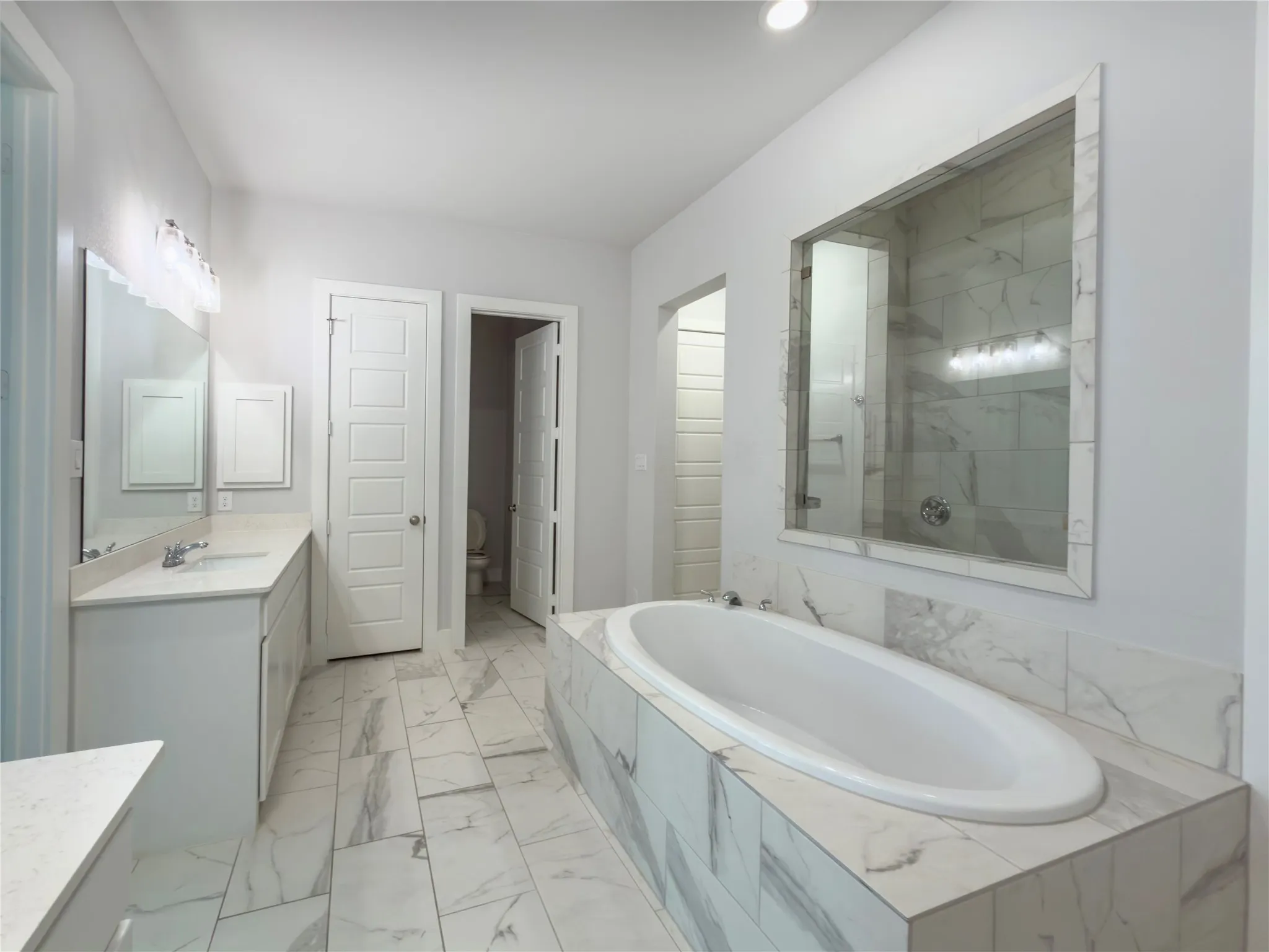Spacious bathroom featuring a built-in soaking tub, a separate glass-enclosed shower, dual vanity sinks with light countertops, and large format marble-look tile flooring