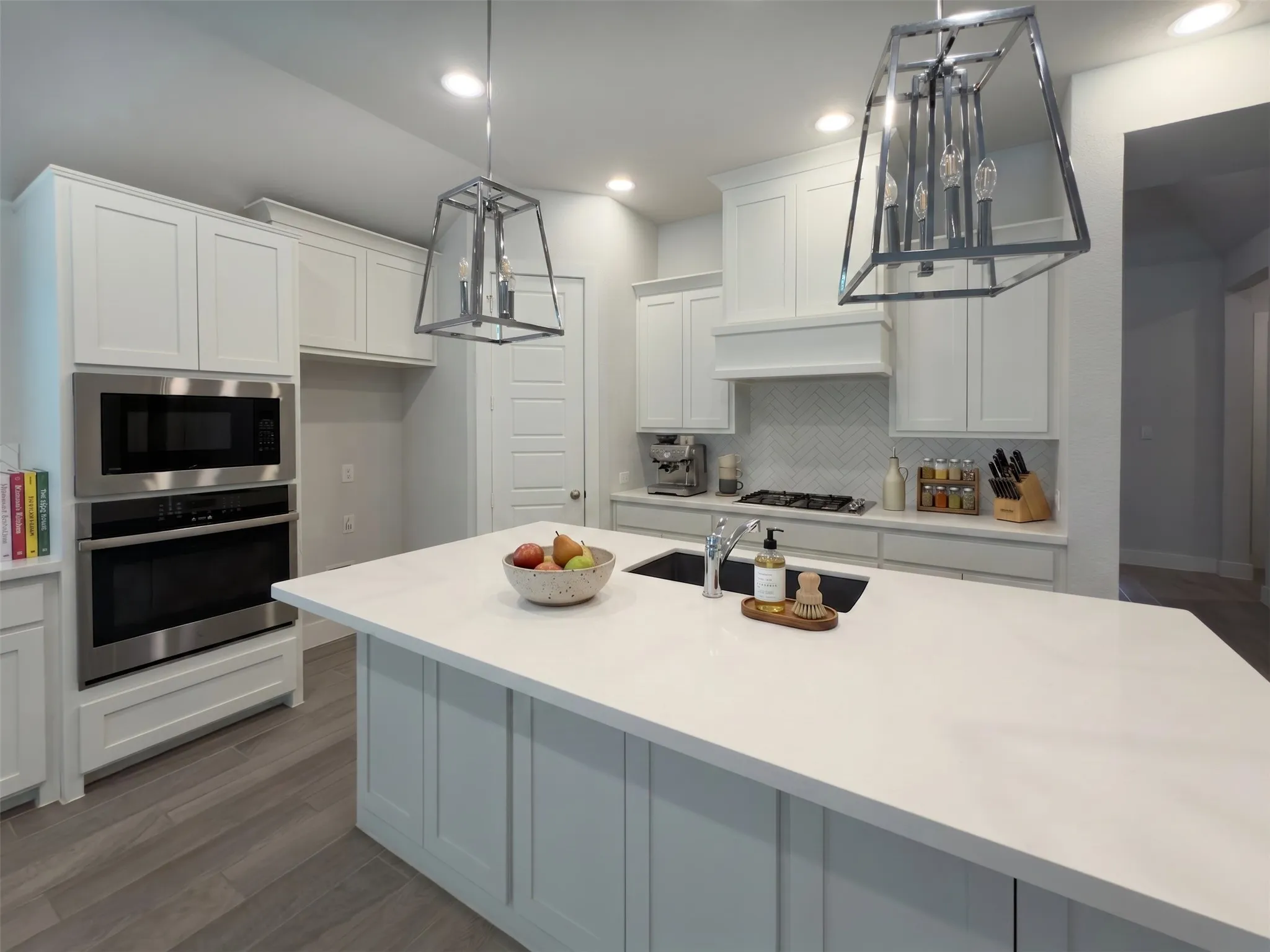 Gourmet kitchen featuring a large island, stainless steel built-in appliances, white shaker cabinetry, a herringbone tile backsplash, and wood-finish flooring