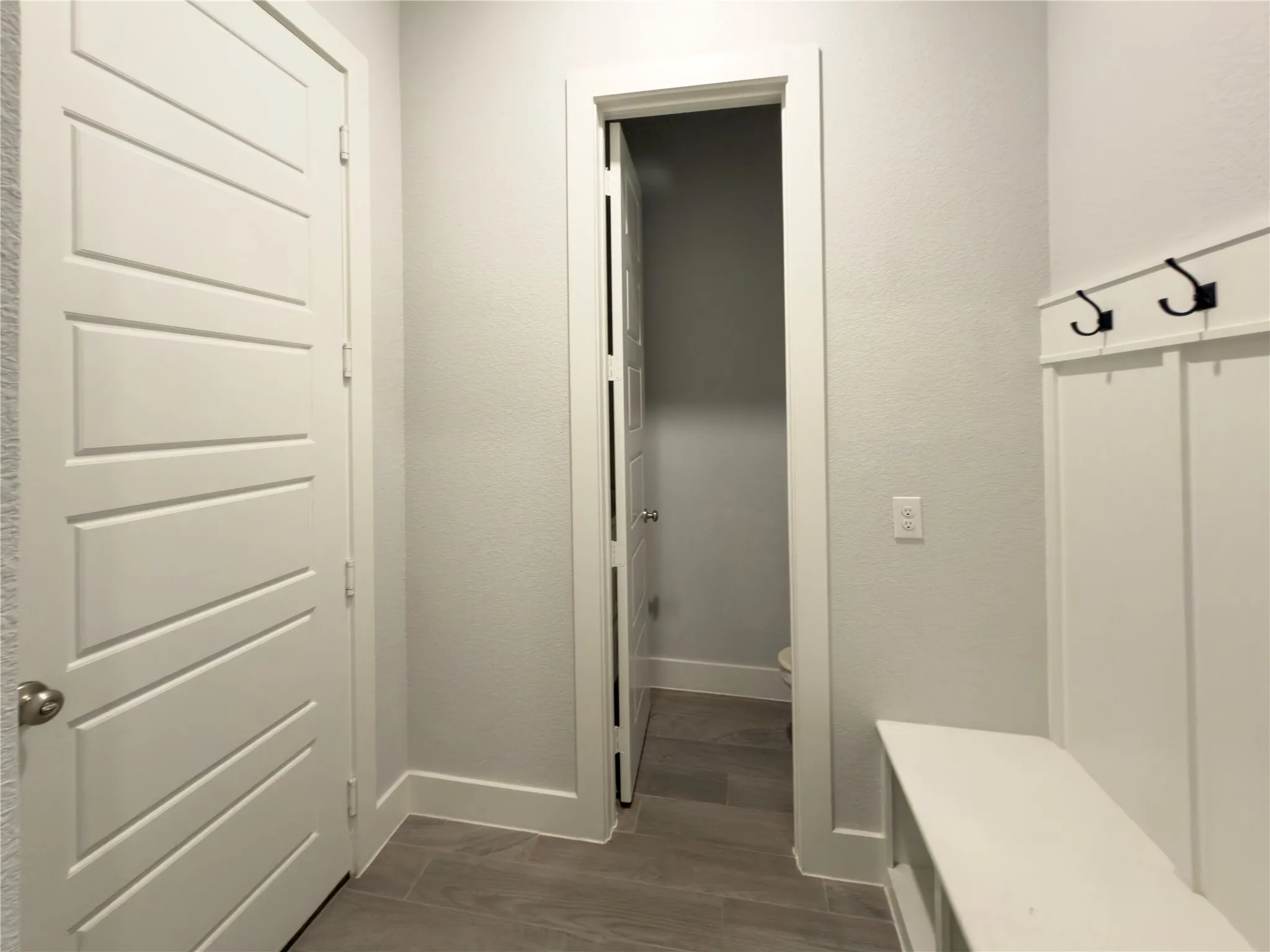 Entryway featuring plank-style tile flooring, white board and batten wall paneling with black hooks, and a built-in bench