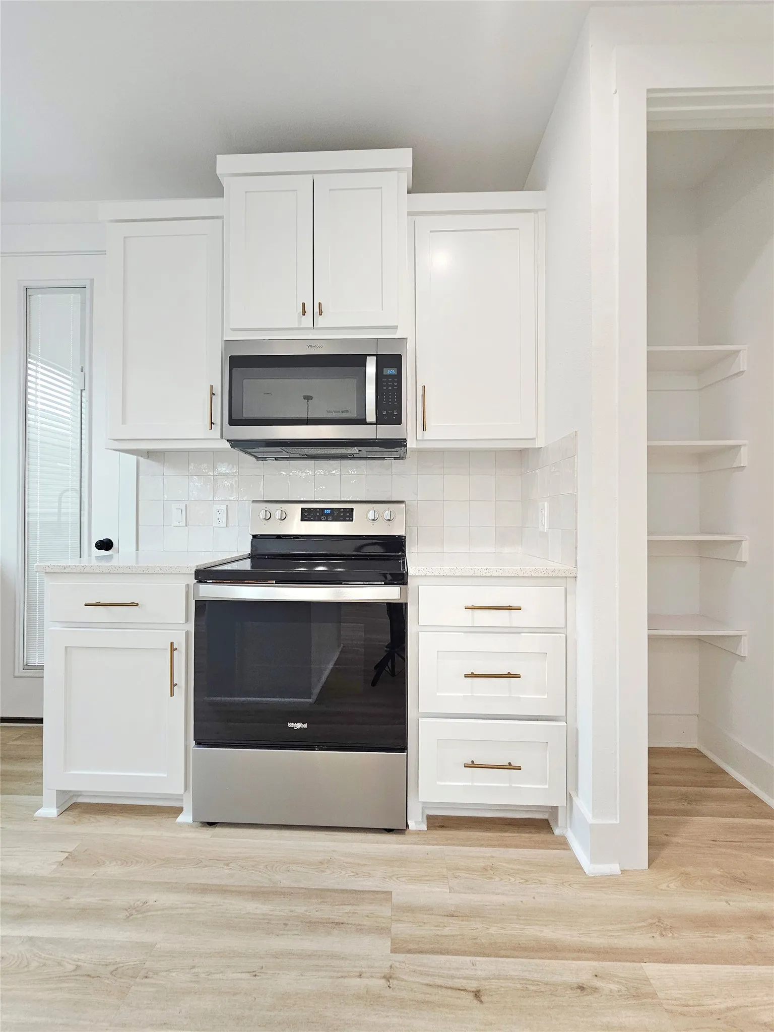 Kitchen featuring appliances with stainless steel finishes, white cabinets, light wood finished floors, backsplash, and baseboards