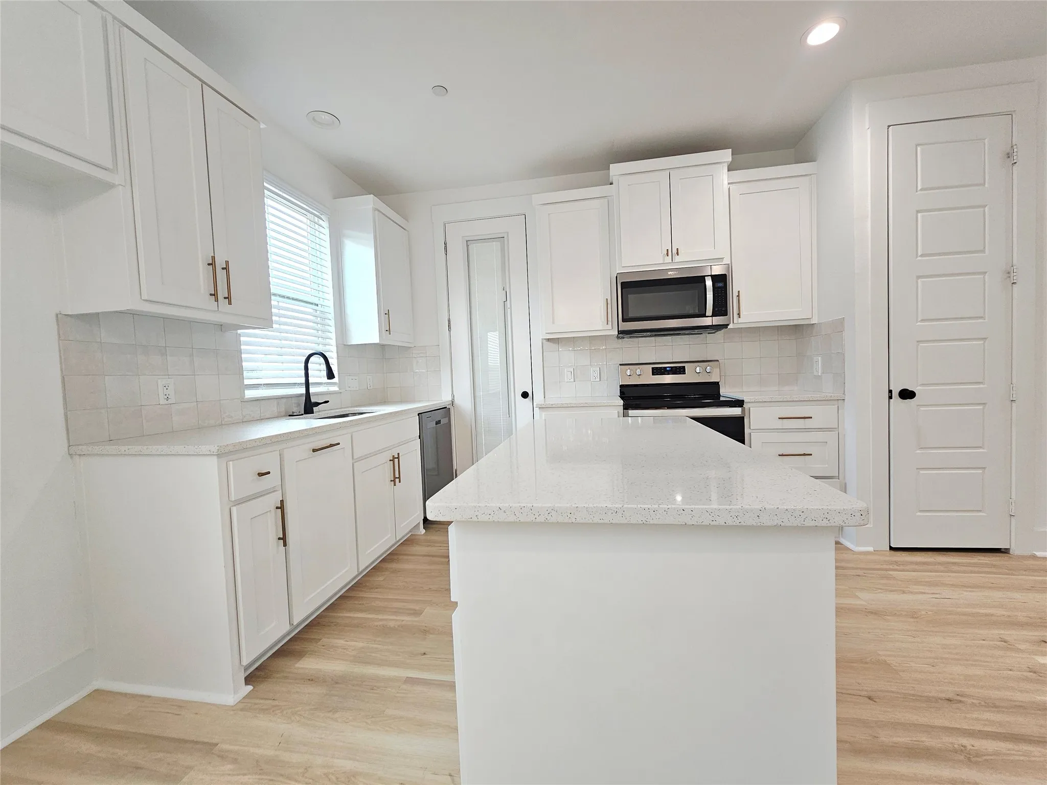Kitchen with stainless steel appliances, a sink, light wood finished floors, a kitchen island, and white cabinetry