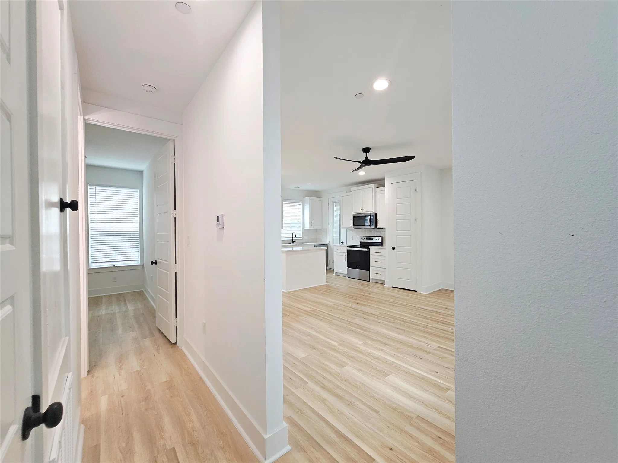 Hall featuring light wood finished floors, healthy amount of natural light, baseboards, recessed lighting, and a sink