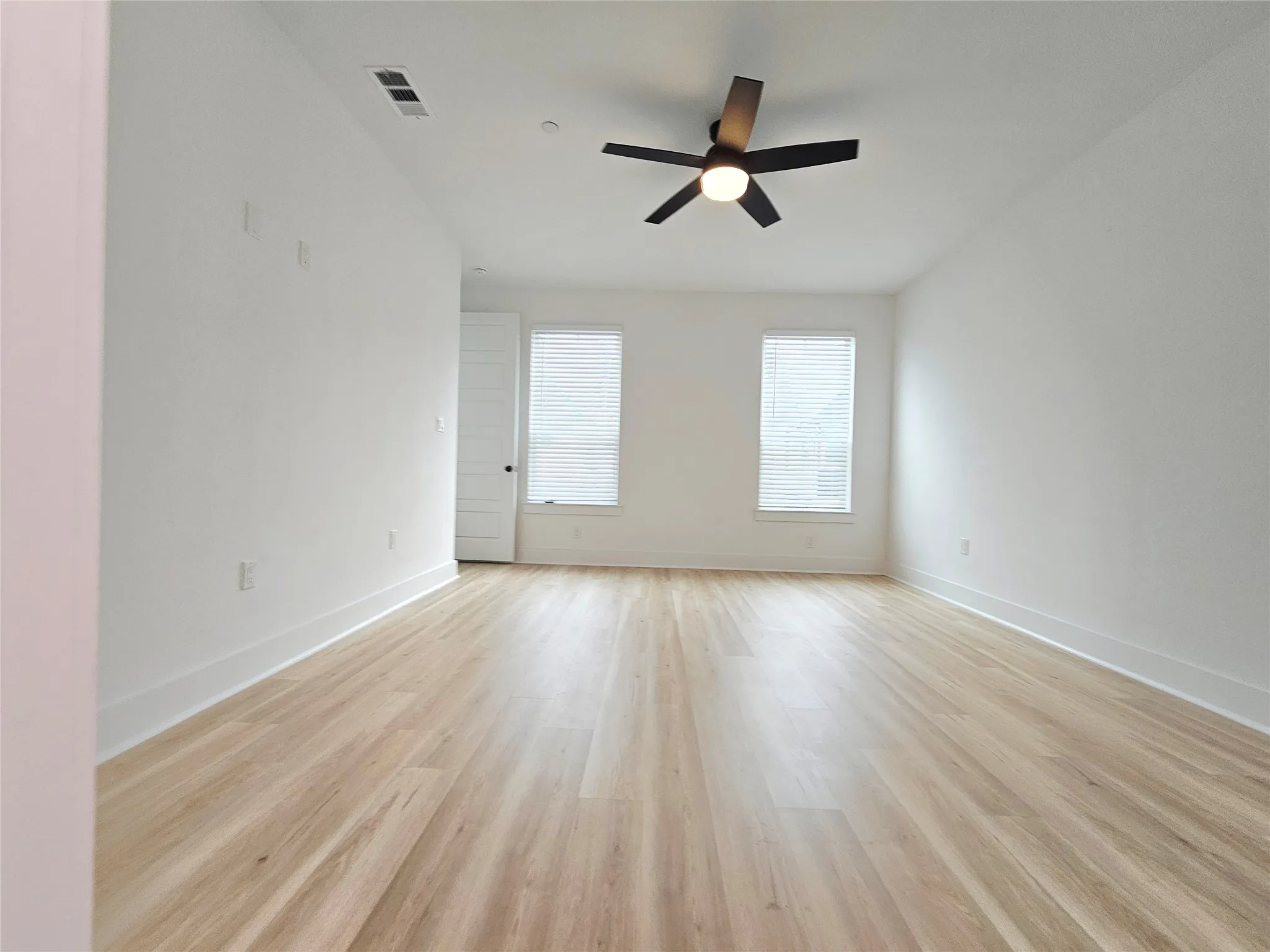 Spare room featuring light wood-style floors, a ceiling fan, and baseboards