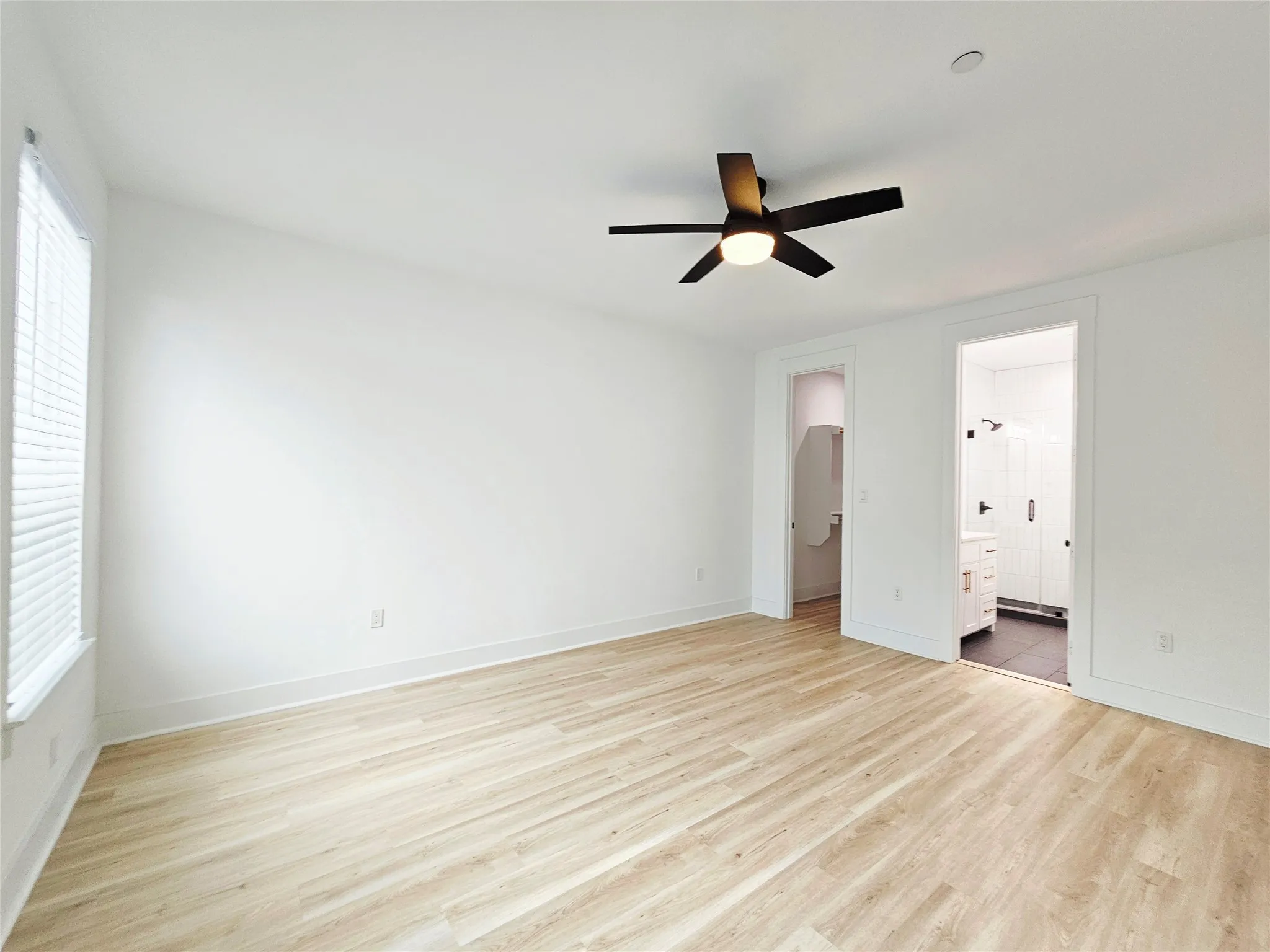 Unfurnished bedroom with light wood-type flooring, multiple windows, ensuite bath, and baseboards