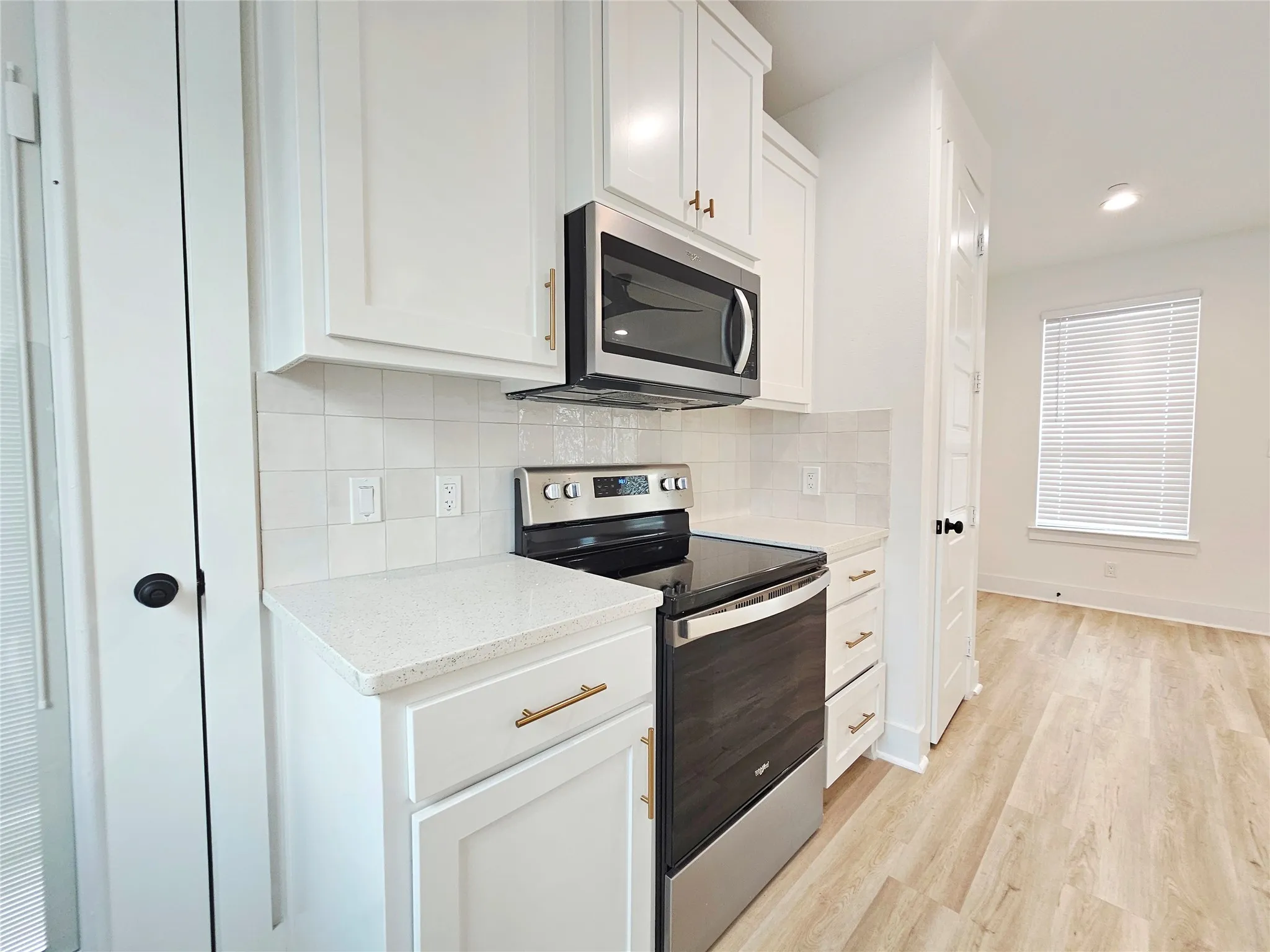 Kitchen with stainless steel appliances, light wood-type flooring, decorative backsplash, white cabinetry, and recessed lighting