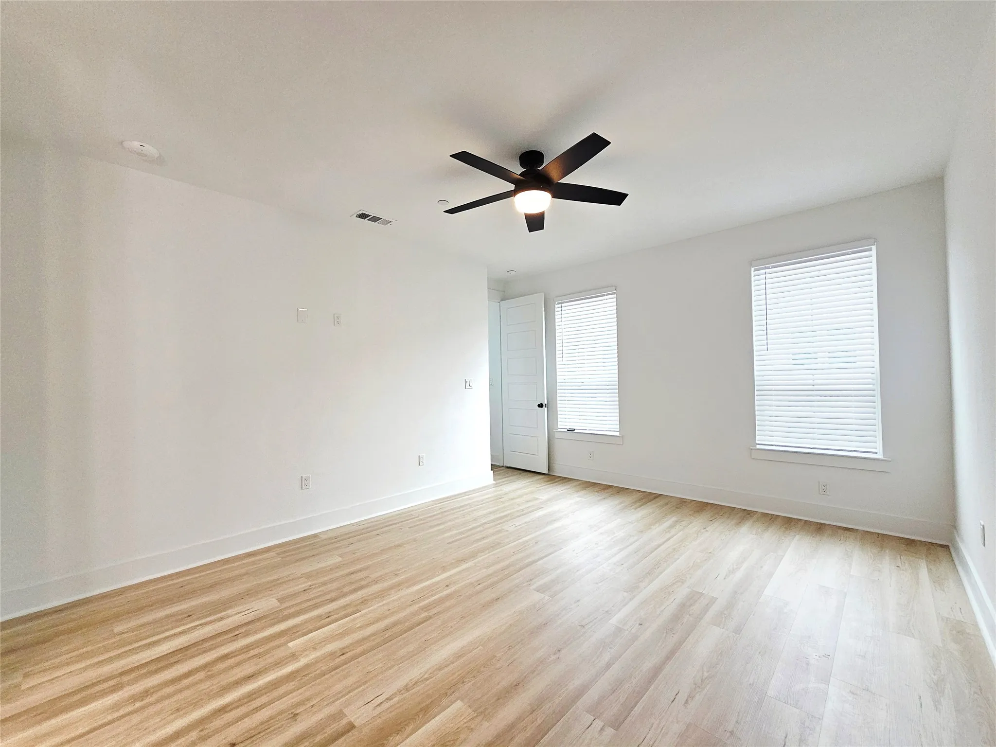 Empty room featuring light wood-type flooring, a ceiling fan, and baseboards