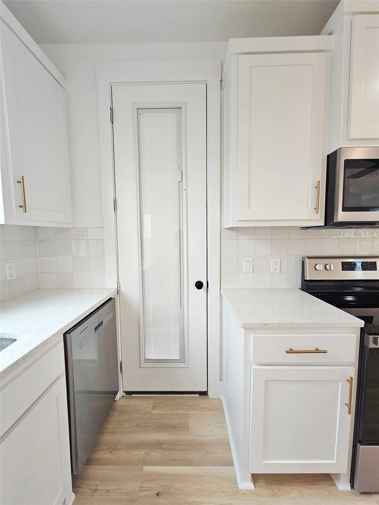 Kitchen featuring appliances with stainless steel finishes, white cabinets, light wood-type flooring, and light stone countertops