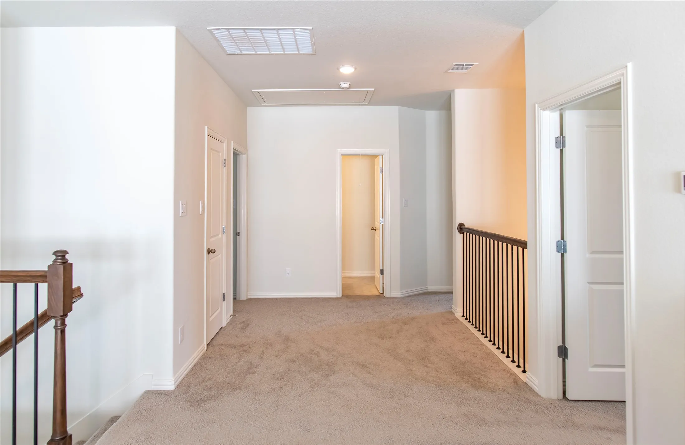 Spacious upper-level landing featuring neutral carpeting, white walls, multiple doorways, and a dark wood and iron baluster railing