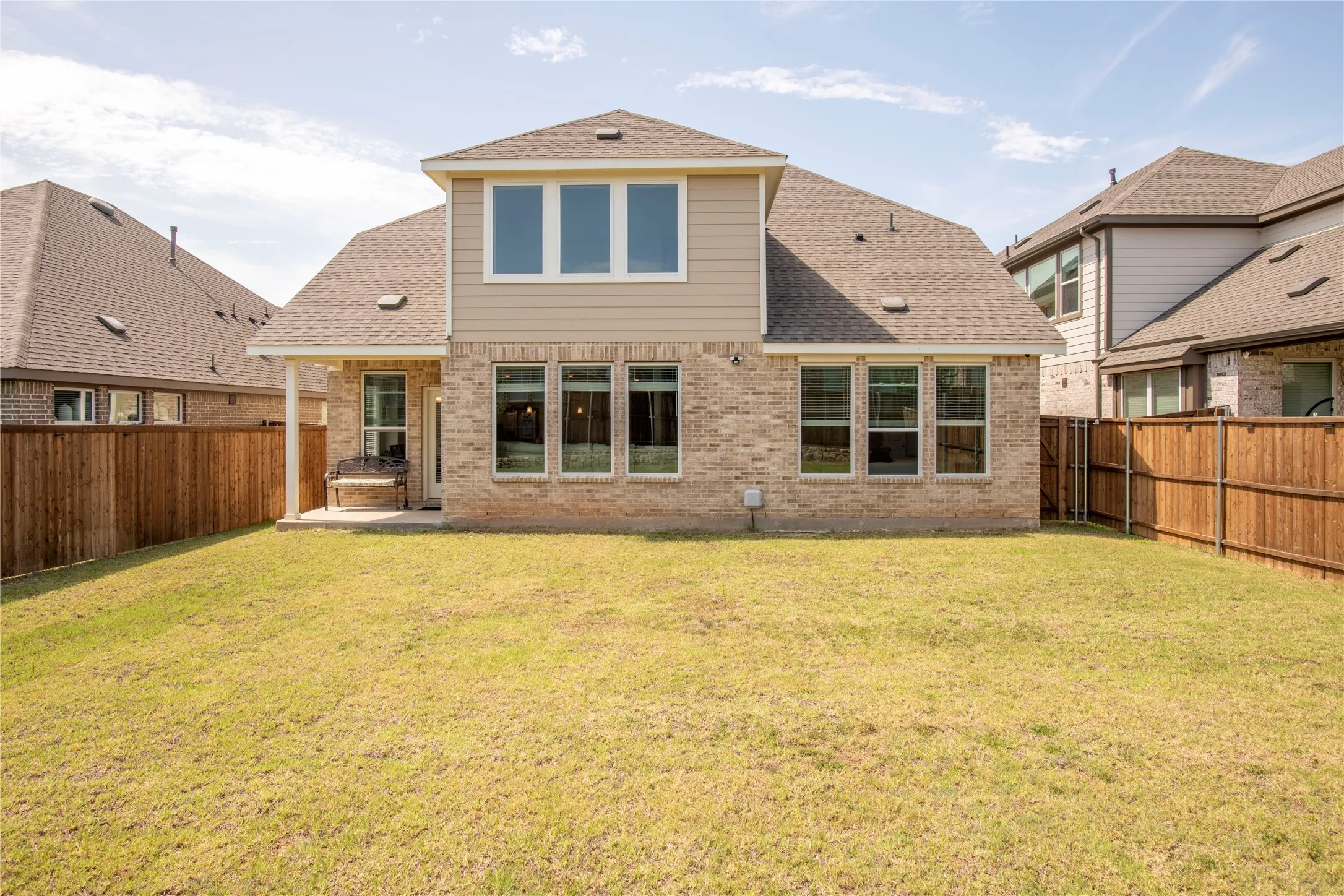 Rear exterior featuring a brick and siding facade, multiple windows, a covered patio, and a fenced yard with a gate