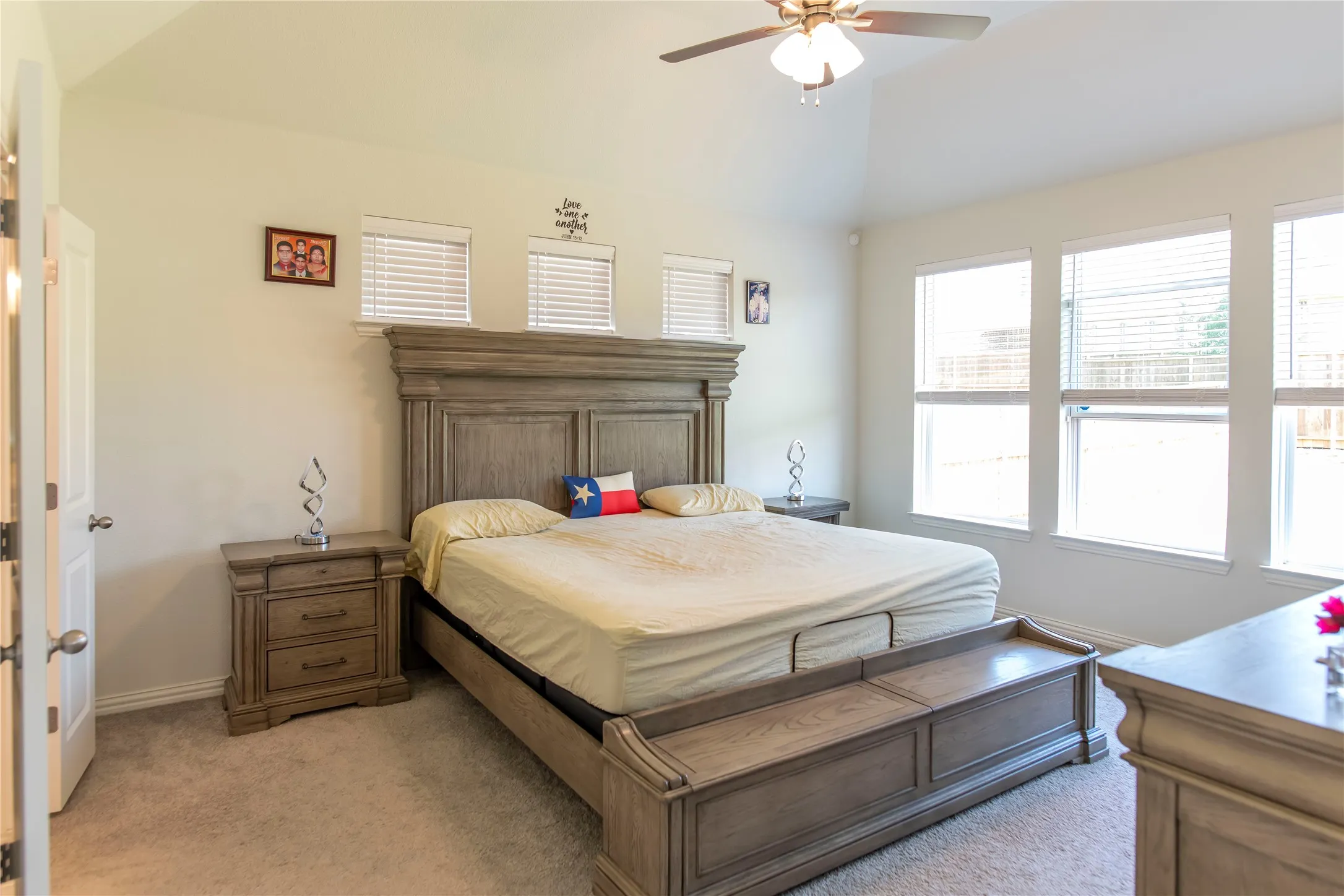 Spacious carpeted room featuring a vaulted ceiling with a ceiling fan, multiple windows with blinds, and light-toned walls