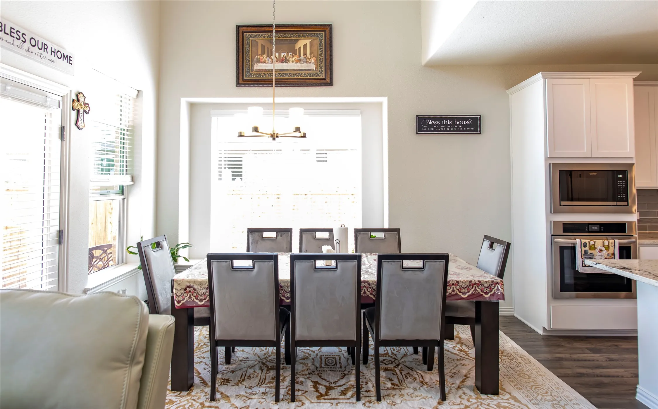 Dining area with high ceilings, featuring a contemporary chandelier, large windows with blinds, and wood-finish flooring