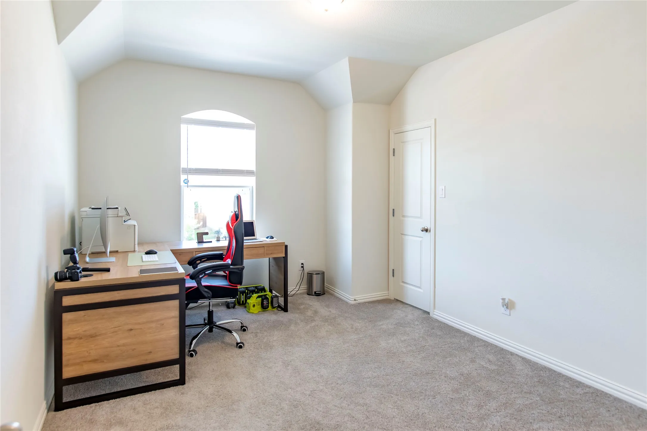 Carpeted room with a vaulted ceiling, an arched window, and a white interior door