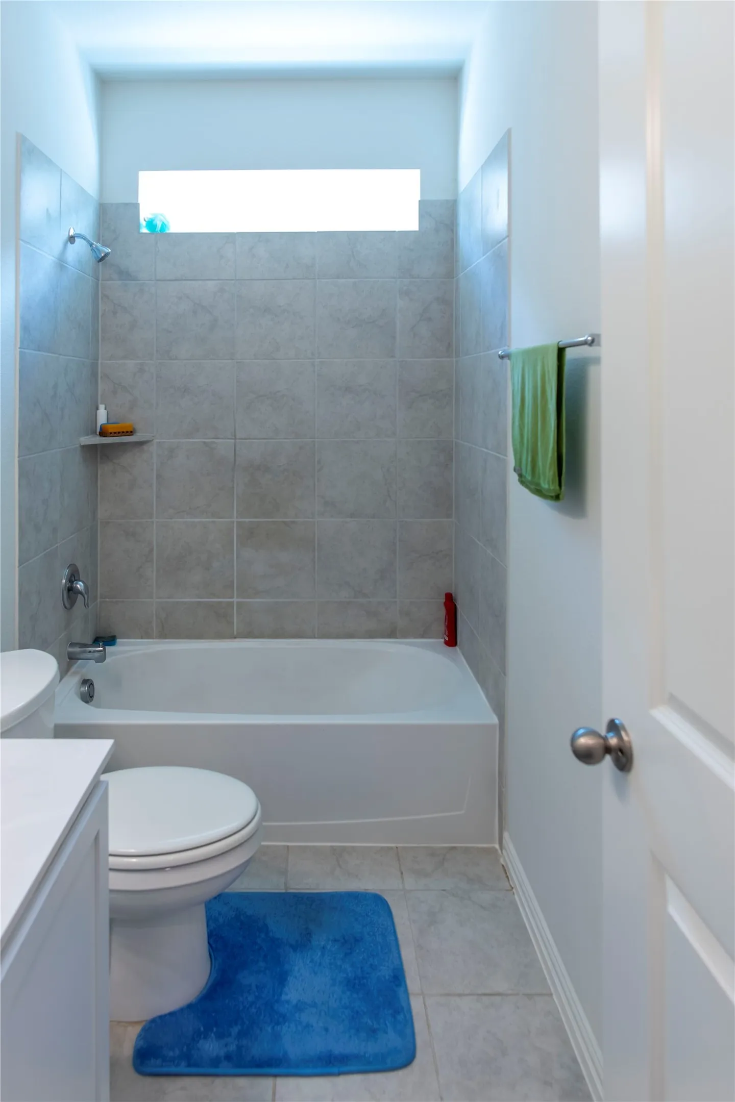 Bathroom featuring a white bathtub, ceramic tile surround with built-in shelf, and a horizontal transom window