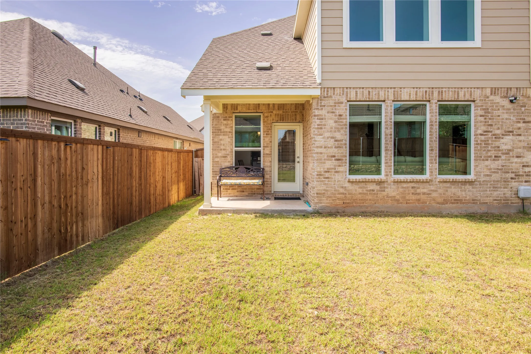 Rear exterior showcasing a covered patio, brick and horizontal siding facade, multiple windows, and a wood privacy fence