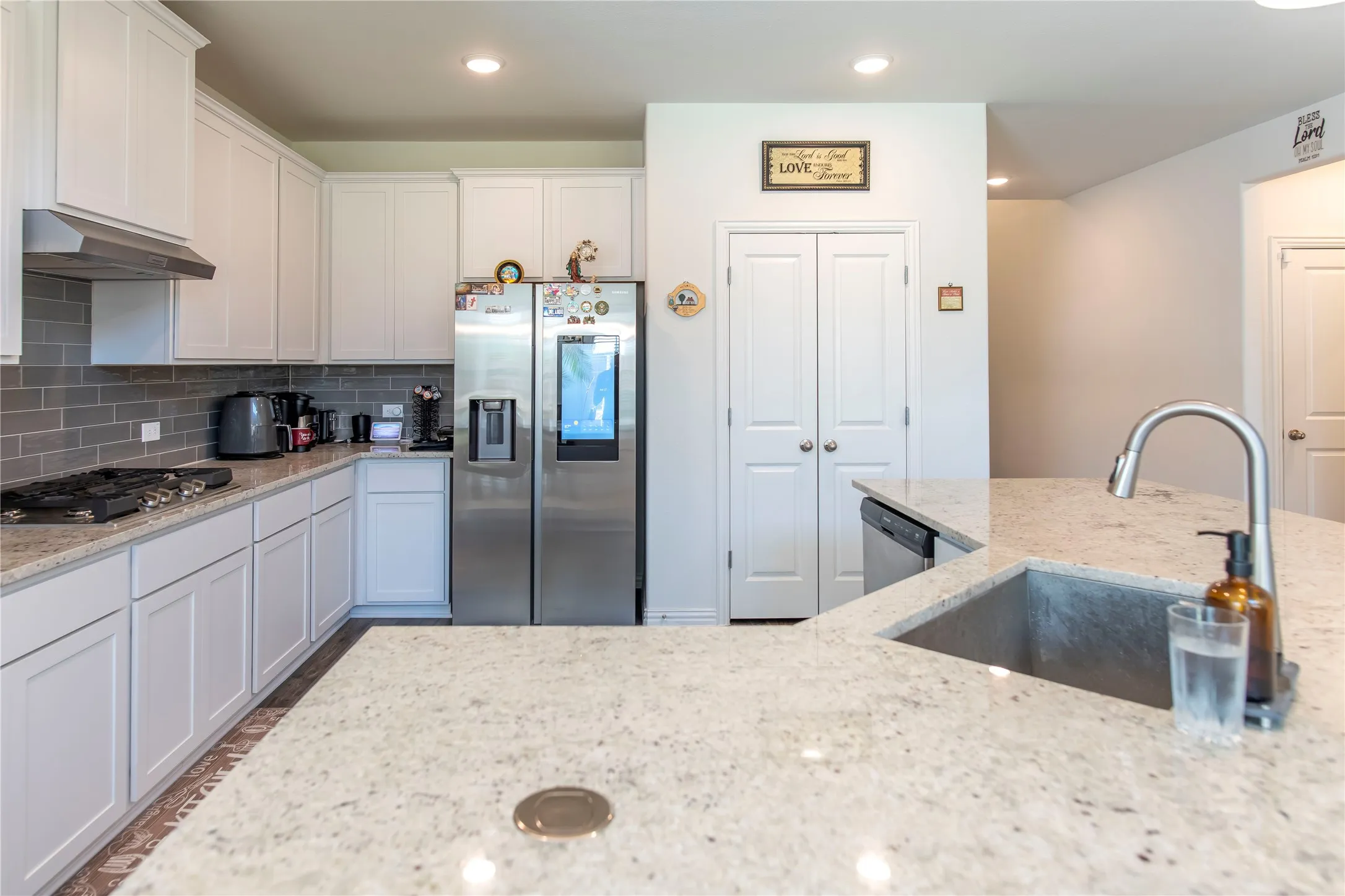 Kitchen featuring white cabinetry, light granite countertops, a stainless steel refrigerator, a gas range with a stainless steel hood, and a gray subway tile backsplash
