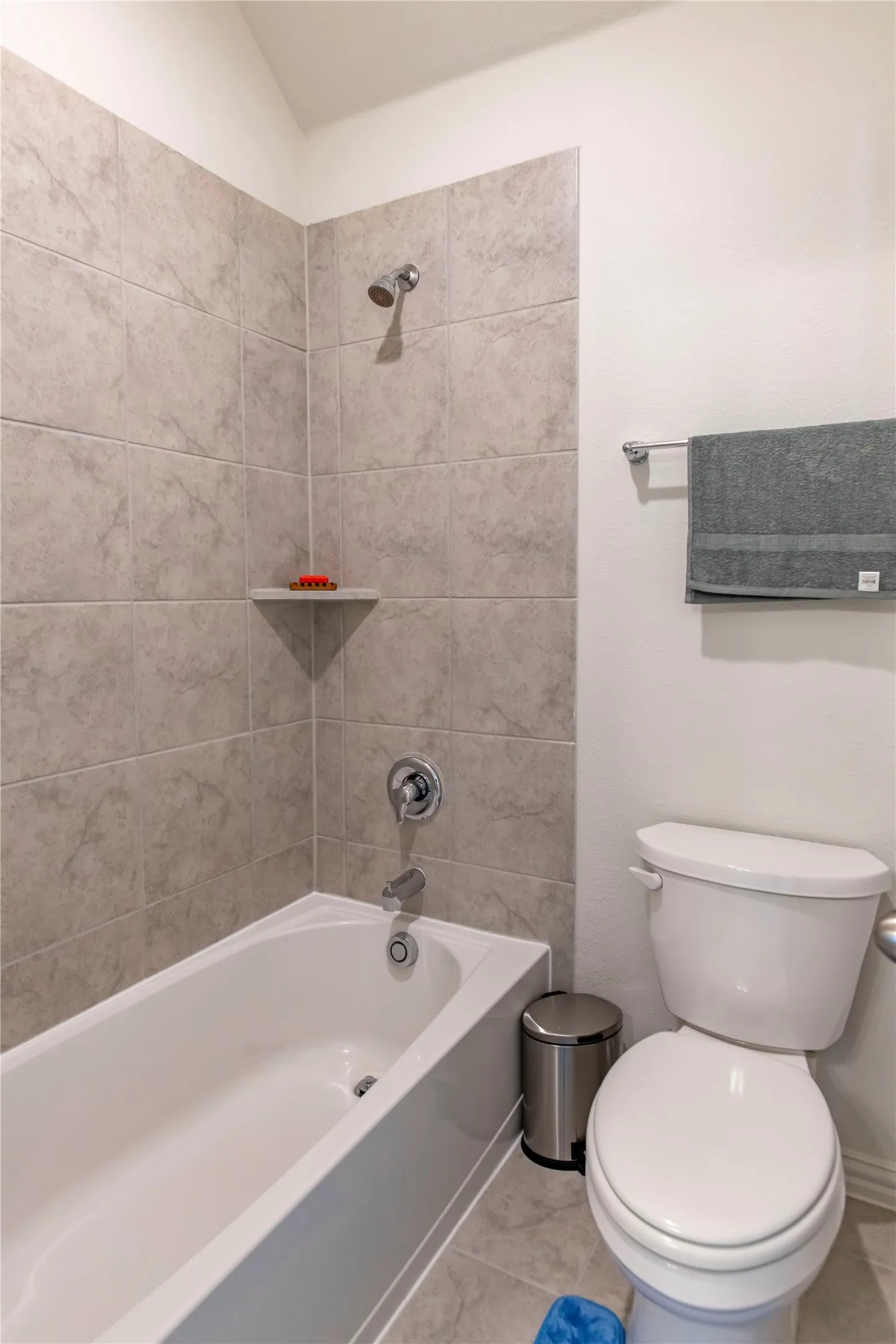 Bathtub and shower combination featuring neutral-toned tile surround, chrome fixtures, and a built-in corner shelf