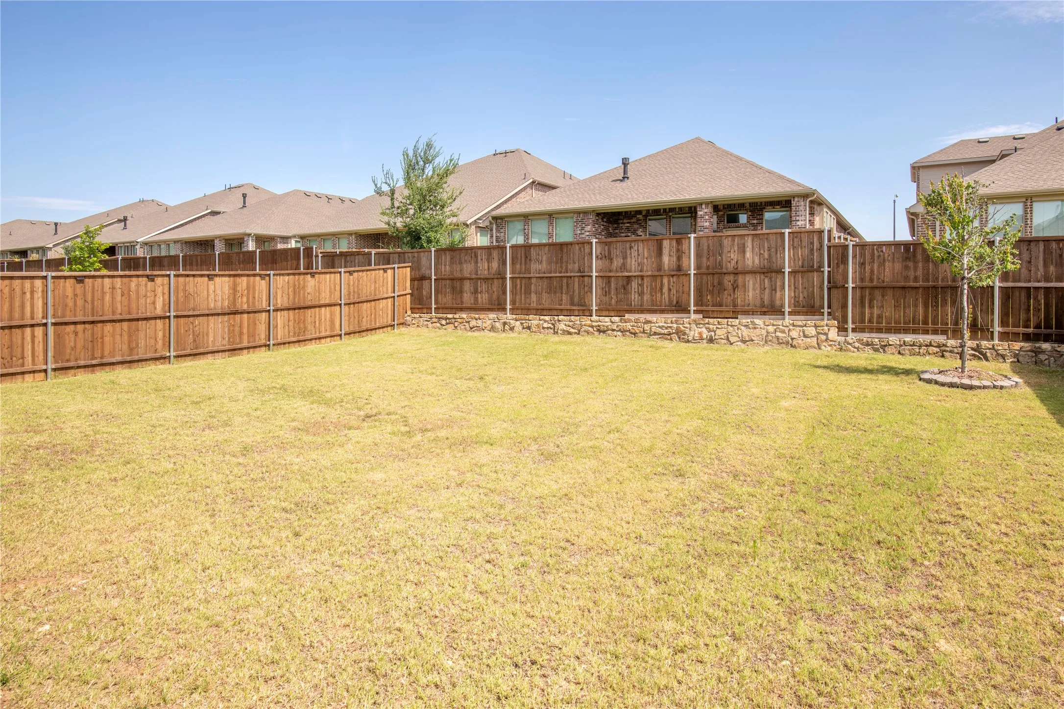 Expansive grassy backyard featuring a stained wood privacy fence and a decorative stone retaining wall