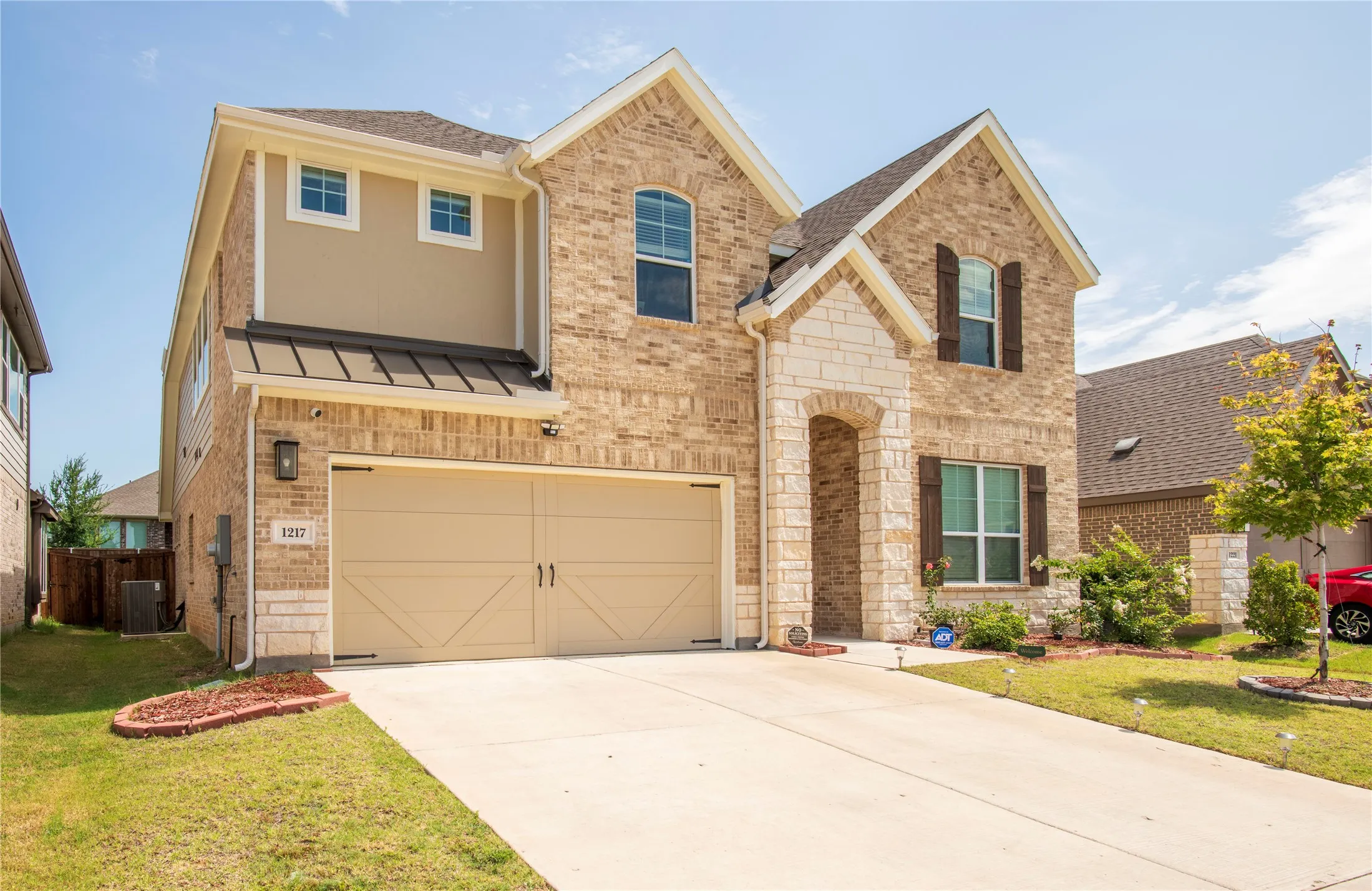 Two-story residence featuring a brick and stone facade, arched entryway, two-car garage with decorative hardware, and wood-toned window shutters