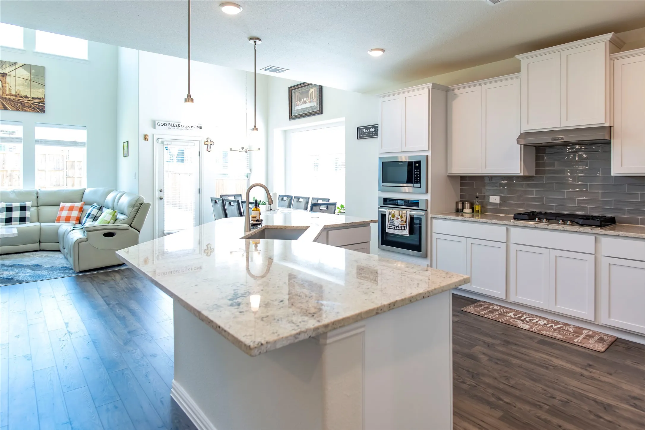 Spacious kitchen featuring a large island with an undermount sink, white cabinetry, a built-in oven and microwave, and a gas cooktop with a gray subway tile backsplash