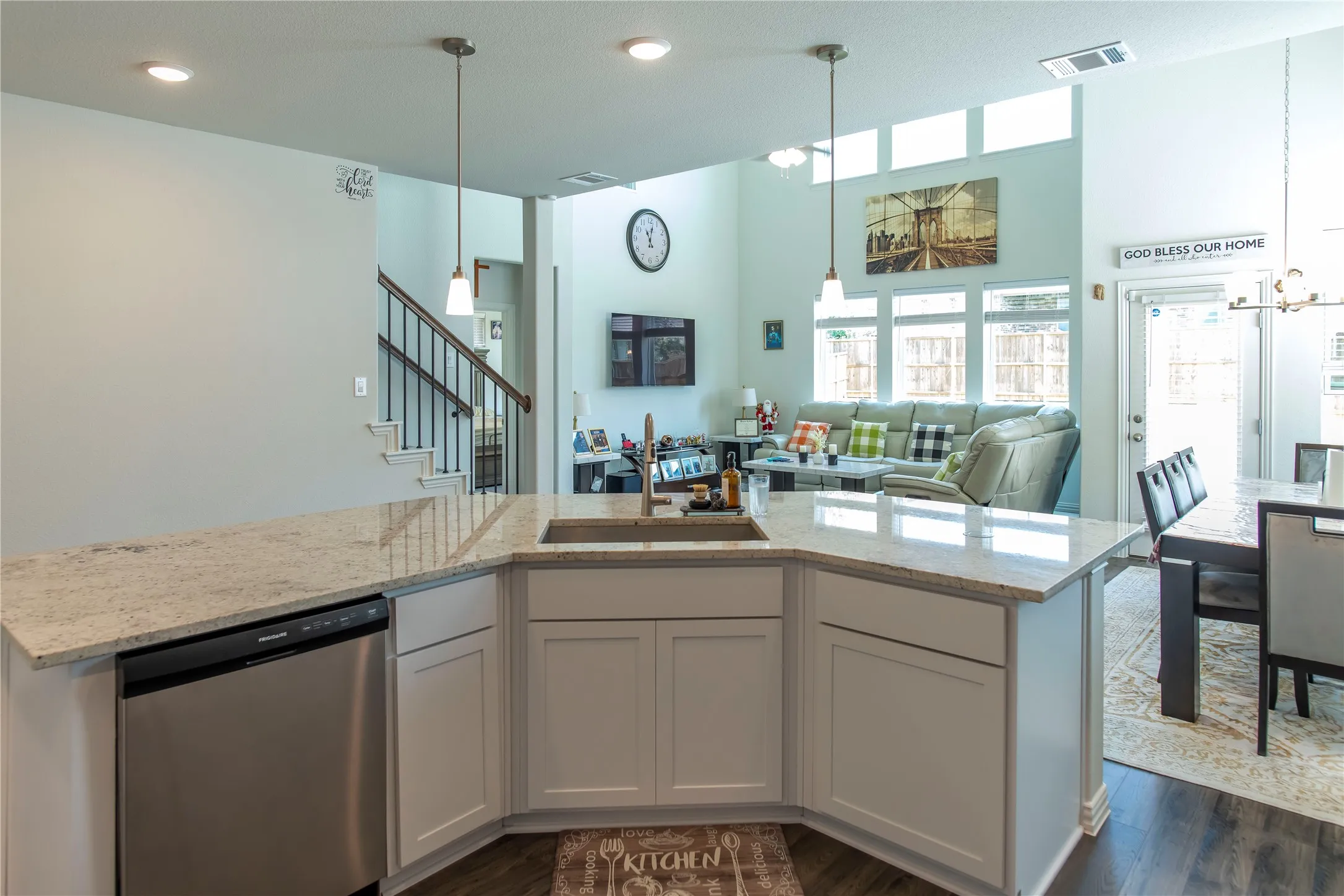 Kitchen island featuring a stainless steel sink, light-colored countertops, white cabinetry, and a built-in stainless steel dishwasher