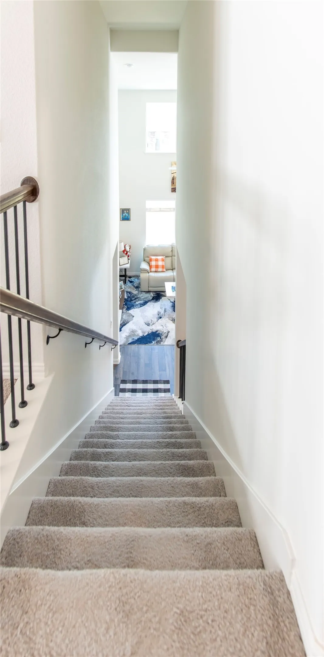 Staircase featuring light gray carpeting, a dark wood-finish handrail, and black metal balusters