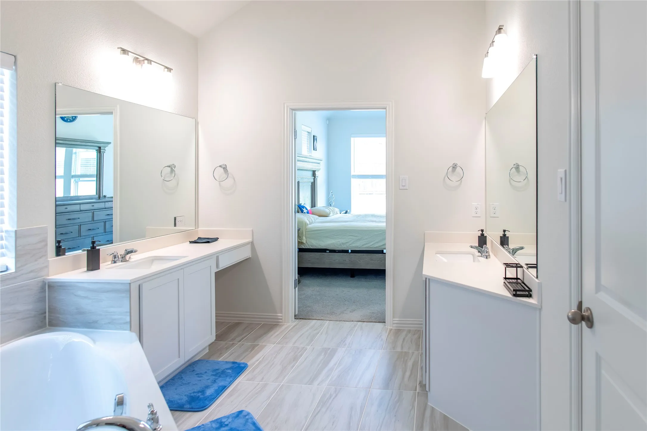 Bathroom featuring dual vanity areas with white cabinetry and integrated sinks, complemented by light-toned tile flooring and a built-in soaking tub