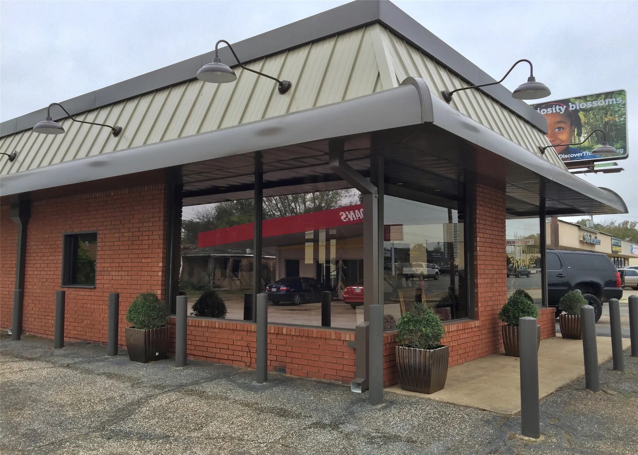 Brick exterior featuring large storefront windows, a corrugated metal roof, and an extended overhead canopy