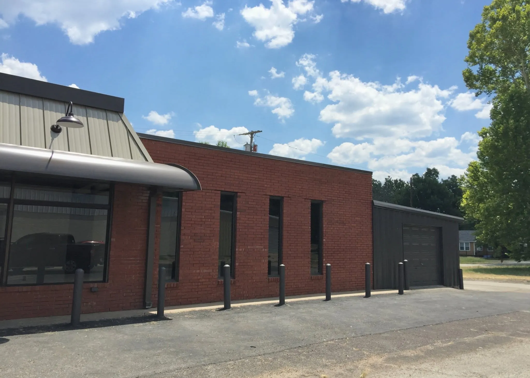 Commercial exterior featuring a brick facade, corrugated metal roofing, a prominent storefront window, and an attached garage bay