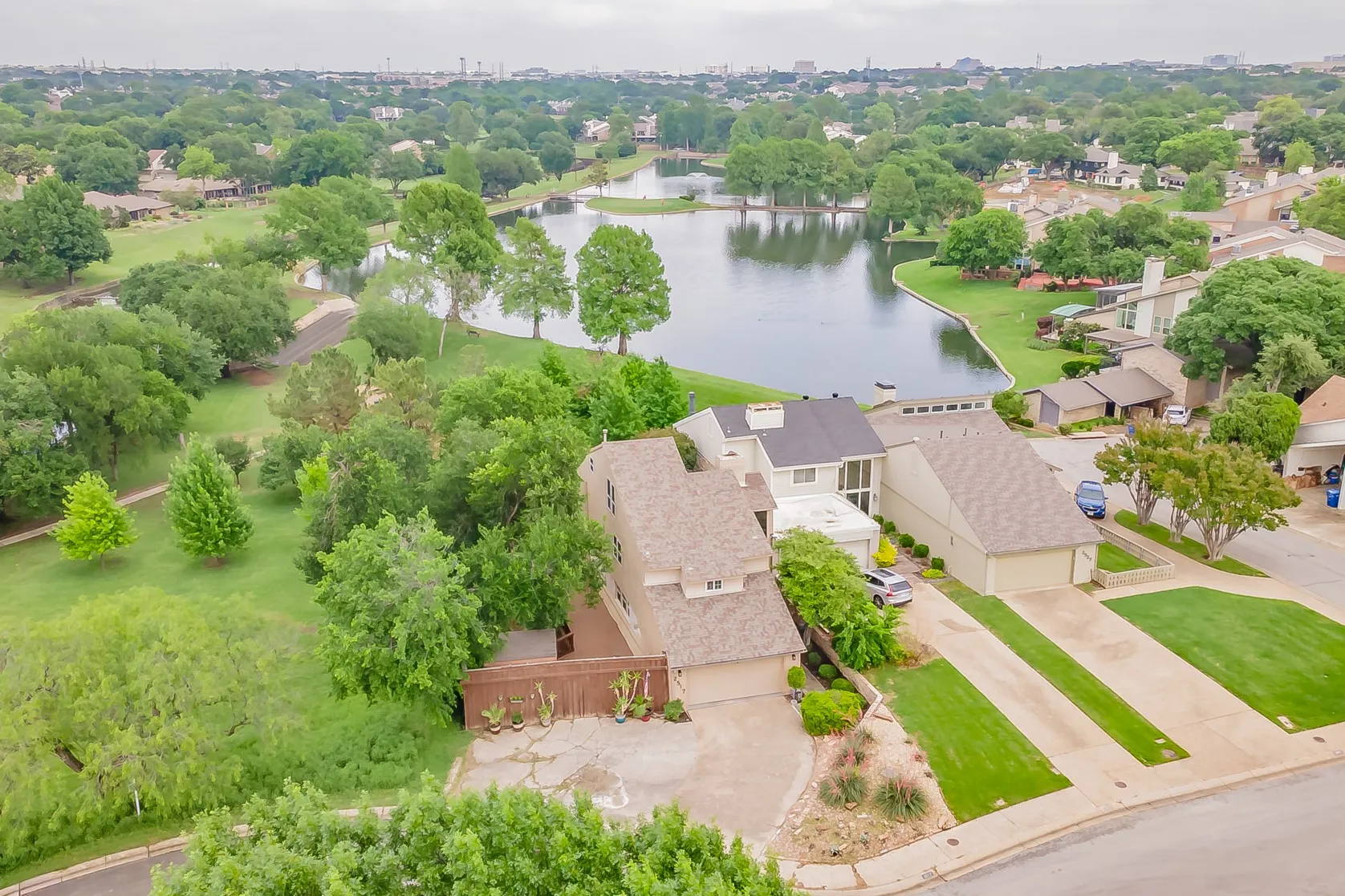 Aerial perspective showcasing a residential property with a shingle roof and an attached garage, situated on a paved driveway