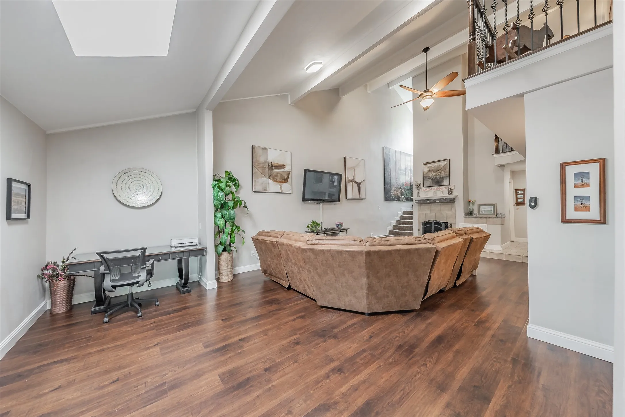 Spacious living area featuring rich wood-finish flooring, a built-in desk, and a stone-faced fireplace with a mantel