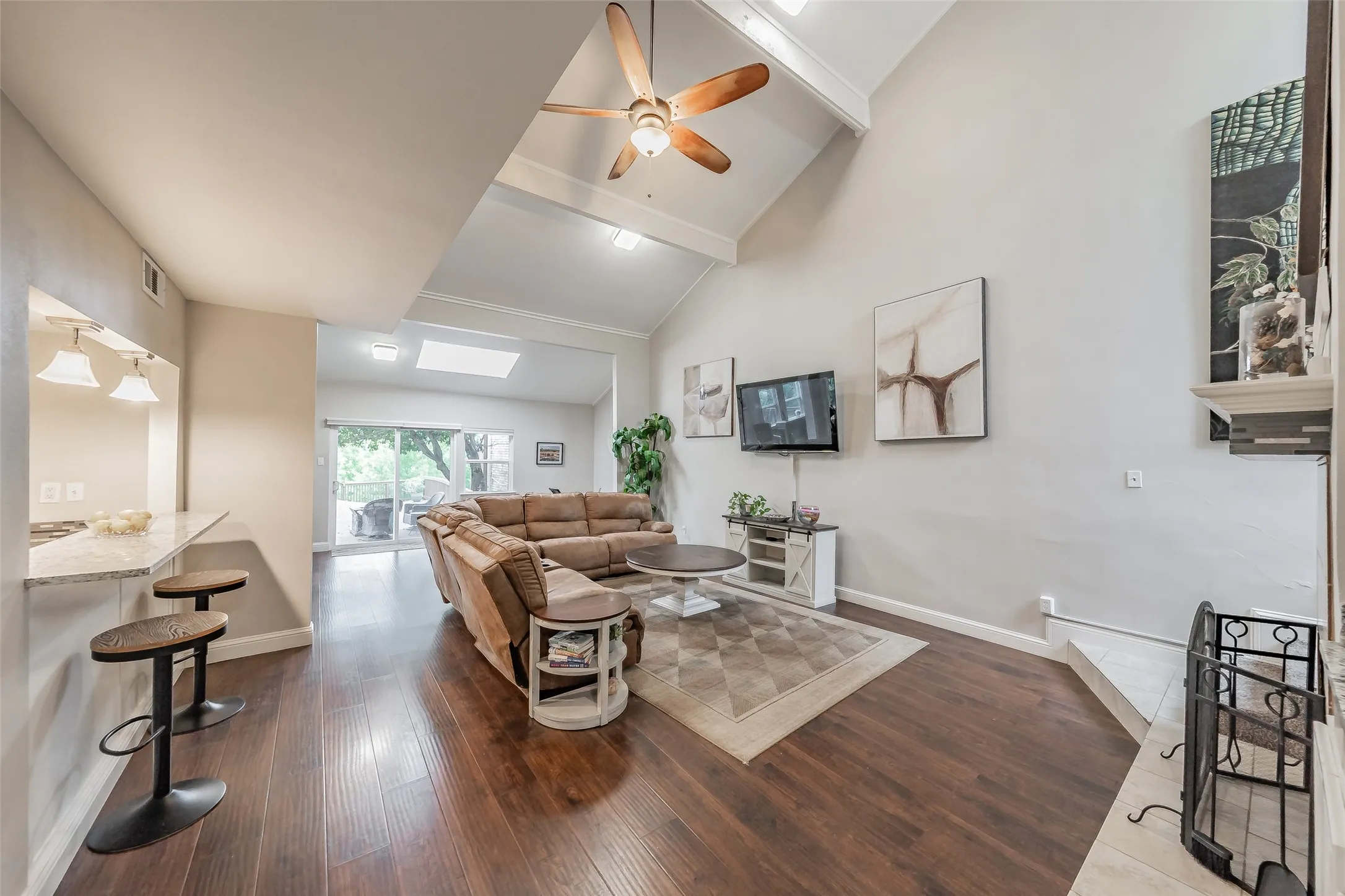 Vaulted ceiling living area featuring dark wood-finish flooring, a built-in fireplace with hearth, and a pass-through bar with a light-colored countertop