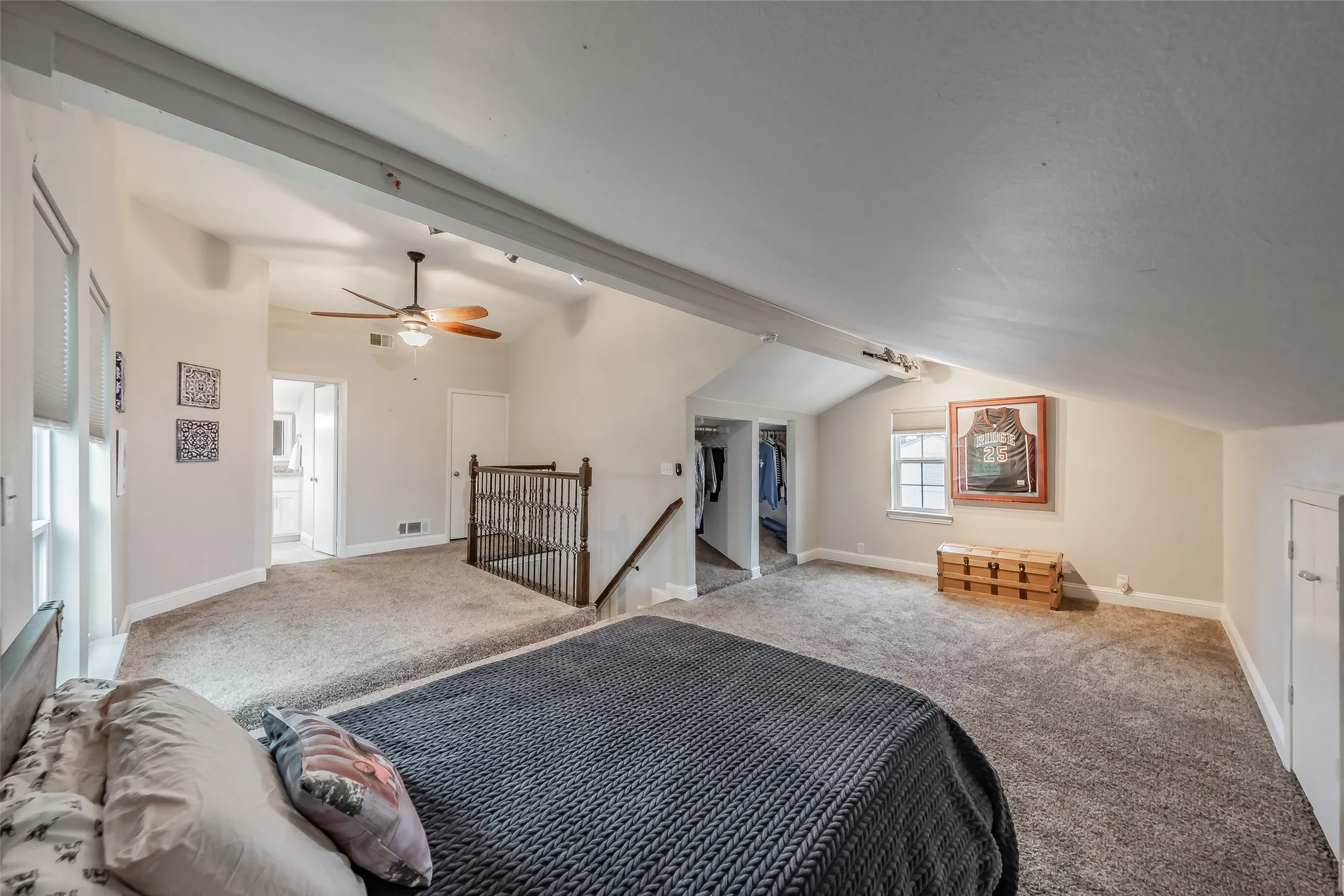 Spacious carpeted room featuring a vaulted ceiling with exposed beams, ceiling fan, multiple windows, and a visible closet area