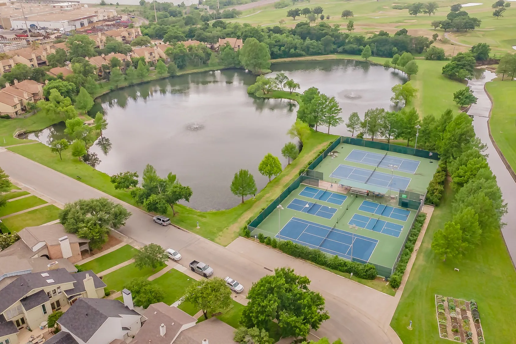Aerial perspective showcasing tennis and pickleball courts with a surrounding fence, positioned by a tranquil pond with water features