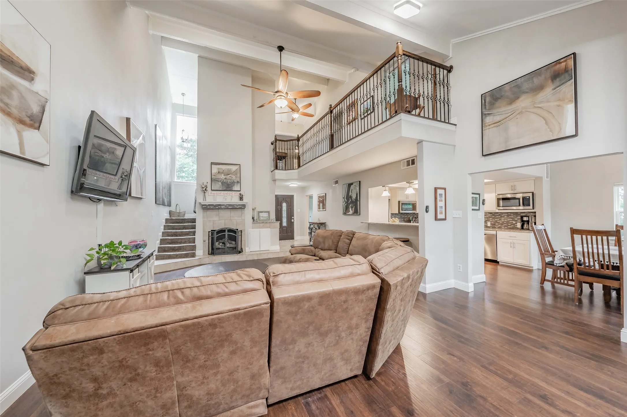 Two-story living area featuring wood-finish flooring, a stone-surround fireplace, a second-story balcony with metal railings, and a ceiling fan