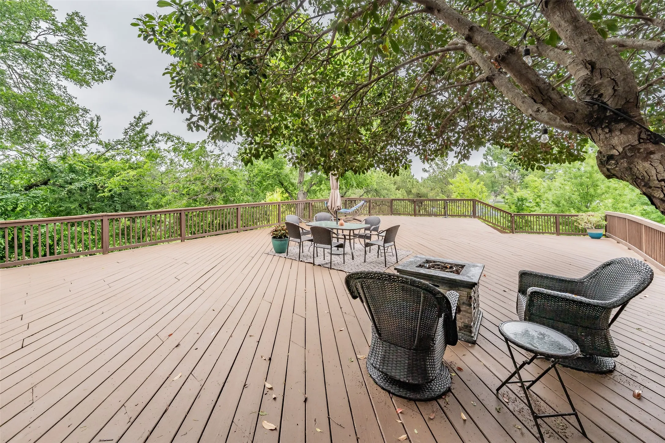 Expansive wood-finish deck with perimeter railing and mature tree canopy