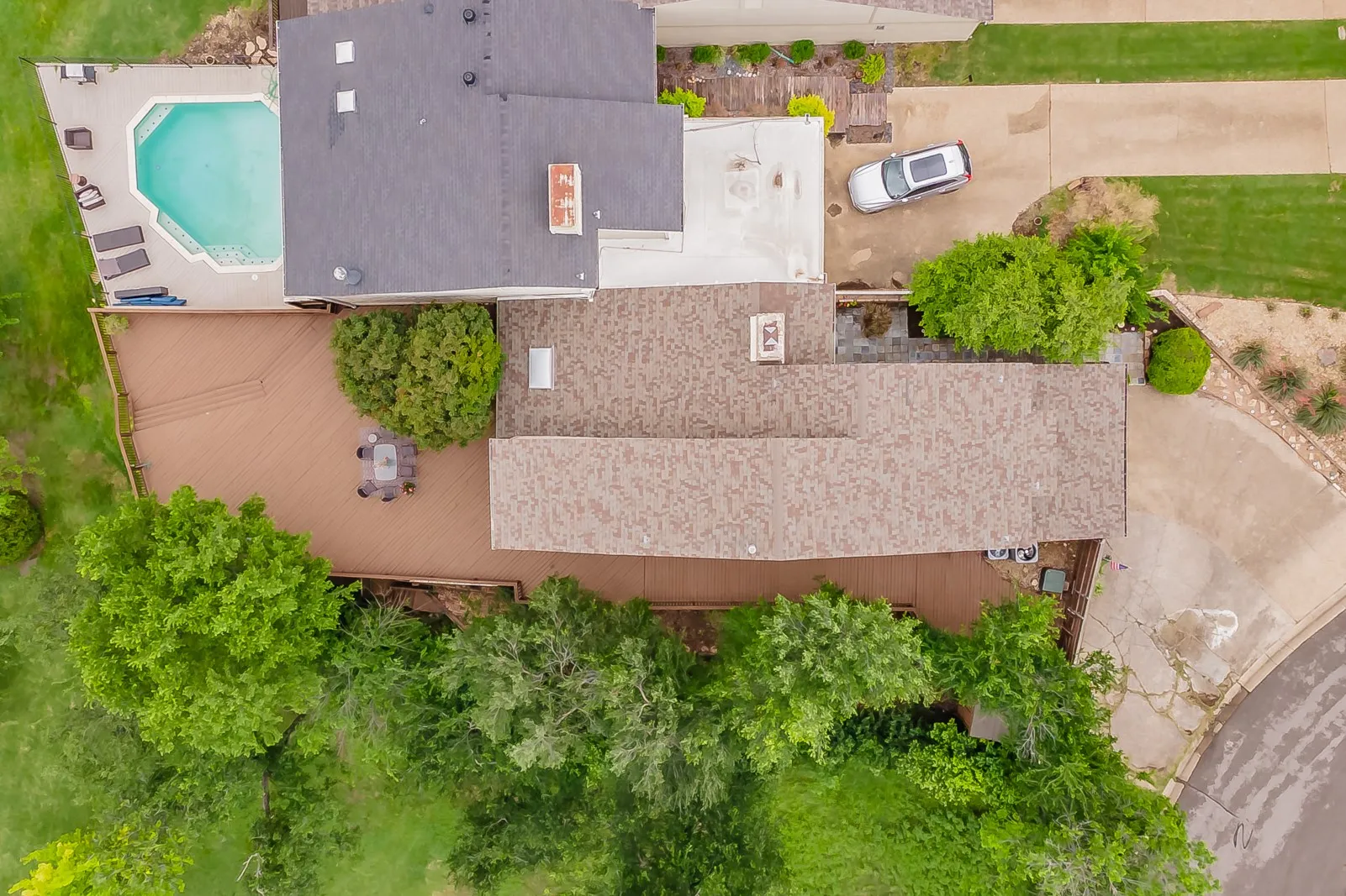 Expansive exterior featuring a geometric in-ground pool, multi-level composite decking, mature landscaping, and an asphalt shingle roof