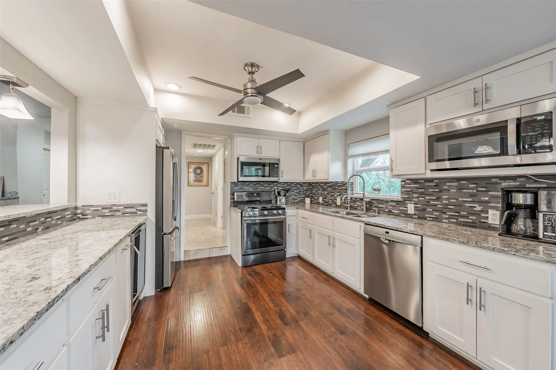 Kitchen featuring wood-finish flooring, white cabinetry with stainless steel hardware, granite countertops, and a mosaic tile backsplash