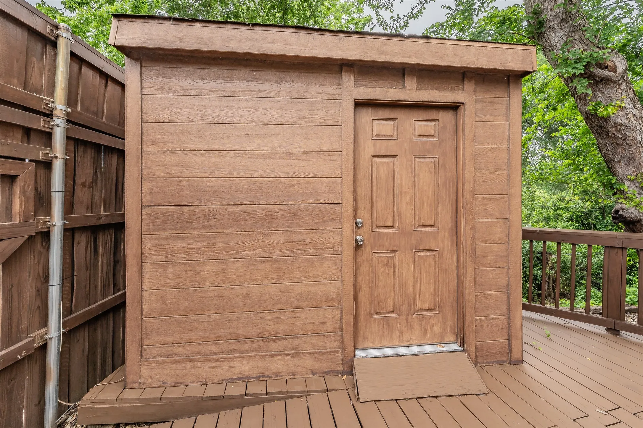 Exterior storage structure featuring wood-finish siding, a paneled door, and a brown entry mat